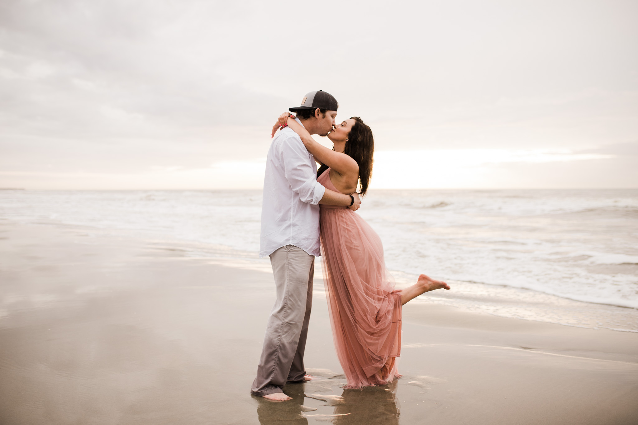 A couple kisses at Folly Beach during an overcast morning engagement session