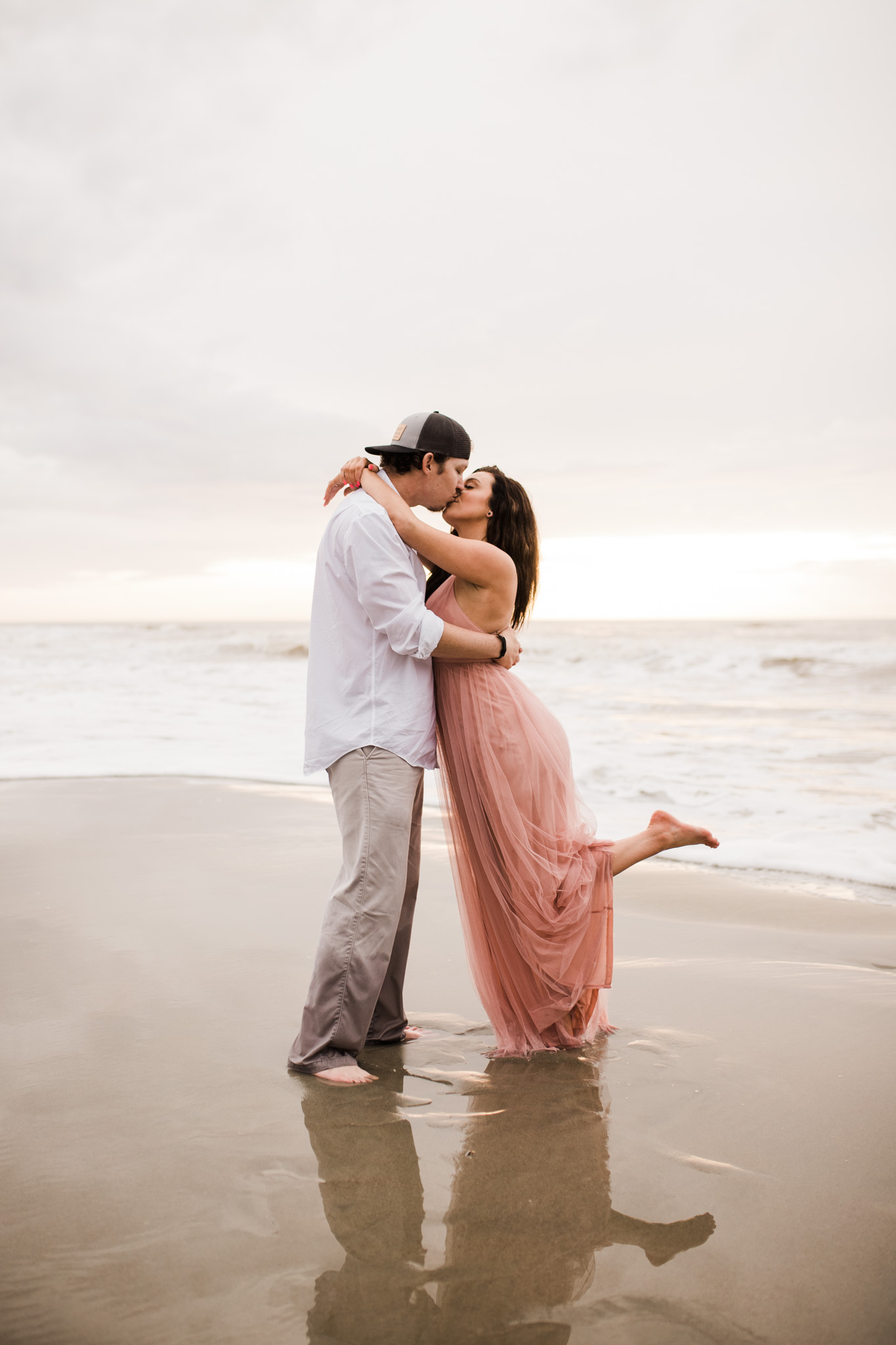 A couple kisses at Folly Beach during an overcast morning engagement session
