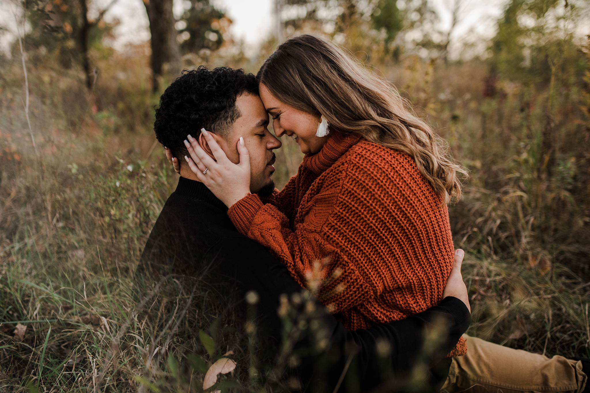 A couple snuggling in a field during their golden hour fall engagement session