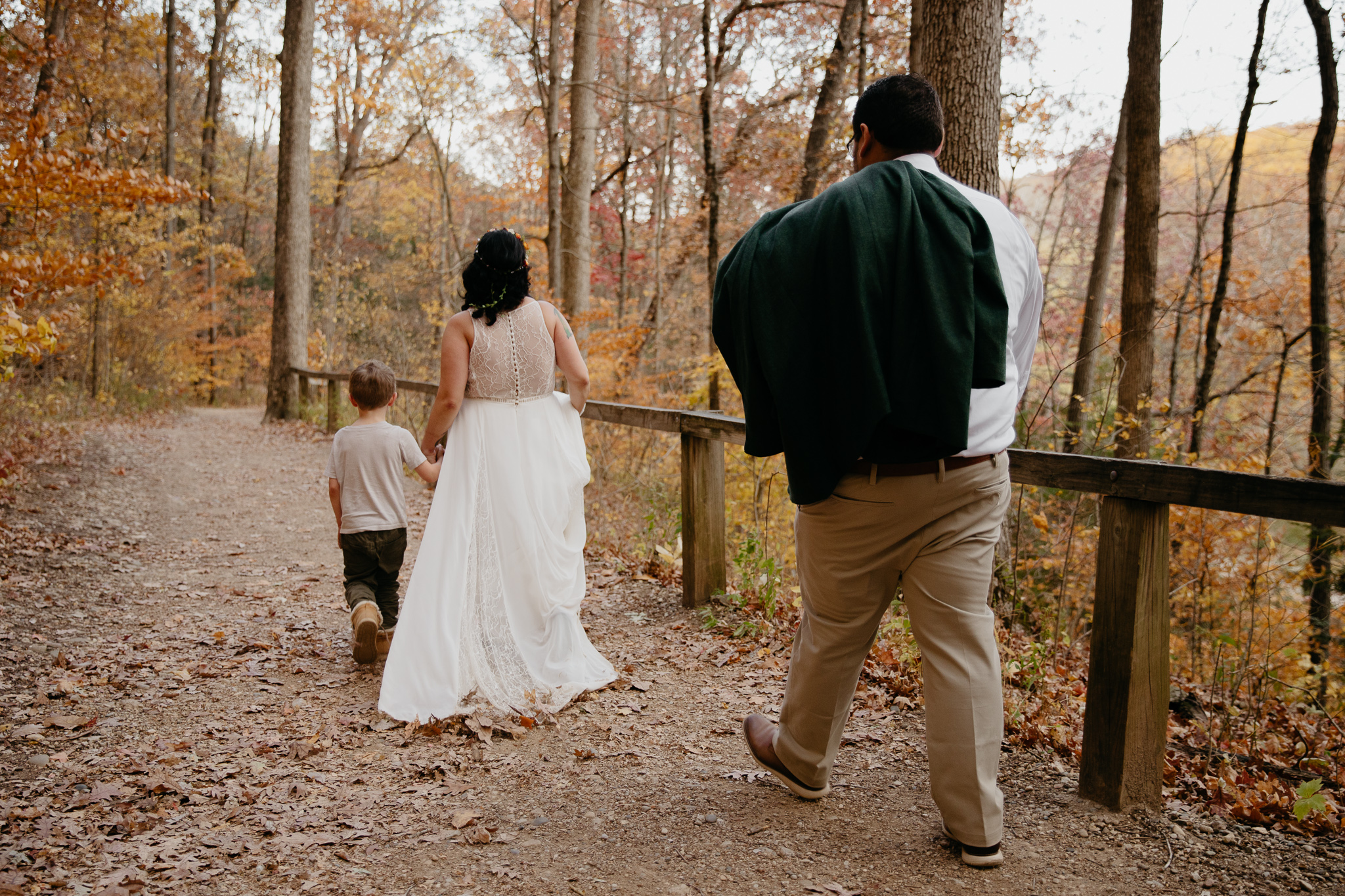Leaves falling as bride and groom hike with their son during their fall elopement at Turkey Run State Park