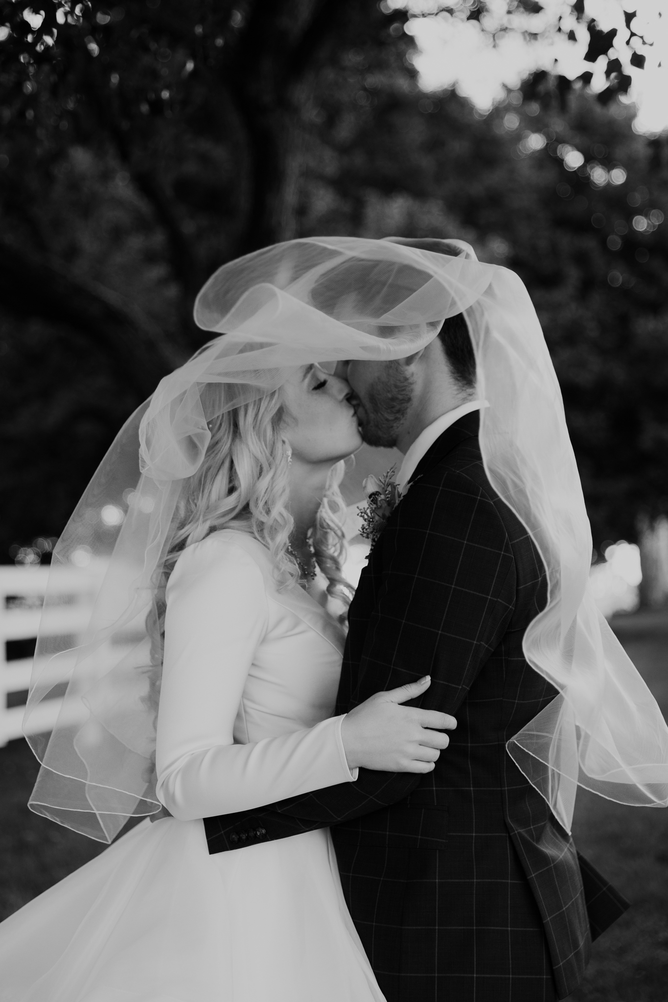 Bride and groom smile at each other and kiss underneath a sheer wedding veil