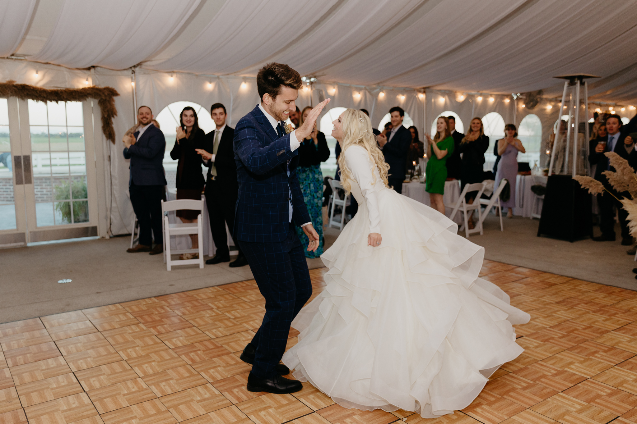 Bride and groom dance hand in hand as they enter their white tent wedding reception in Oswego, IL