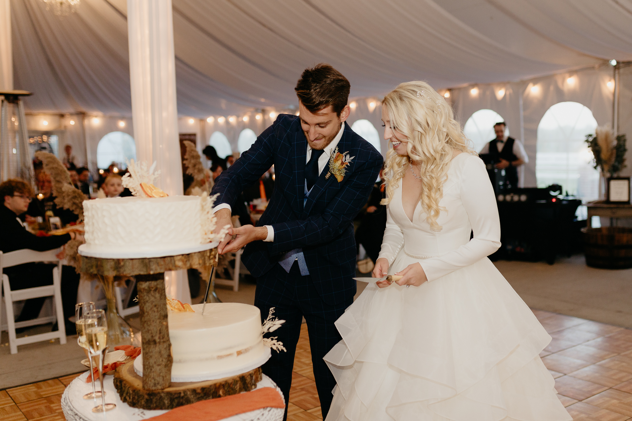 Bride and groom cut cake together in a white tent during their October wedding reception