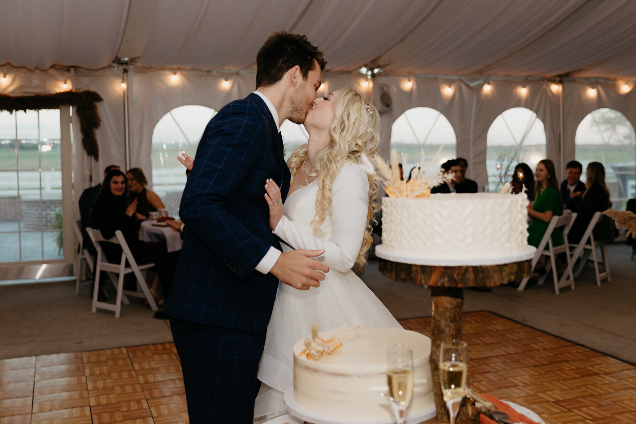 Bride and groom cut cake together in a white tent during their October wedding reception