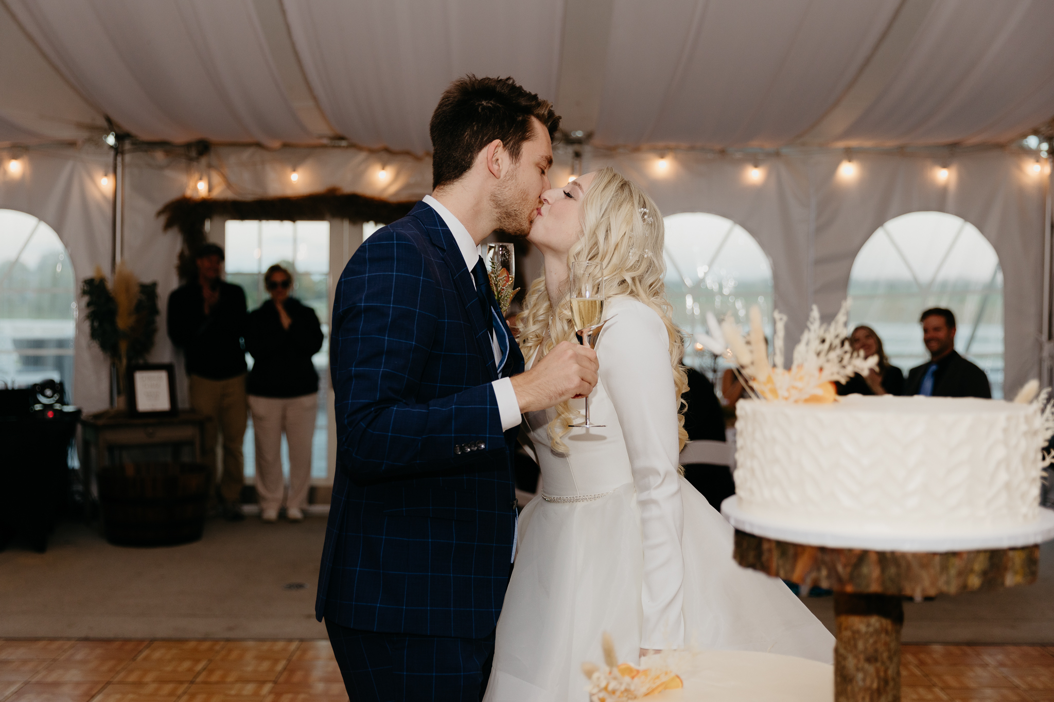 Bride and groom toast champagne and kiss in a white tent during their October wedding reception