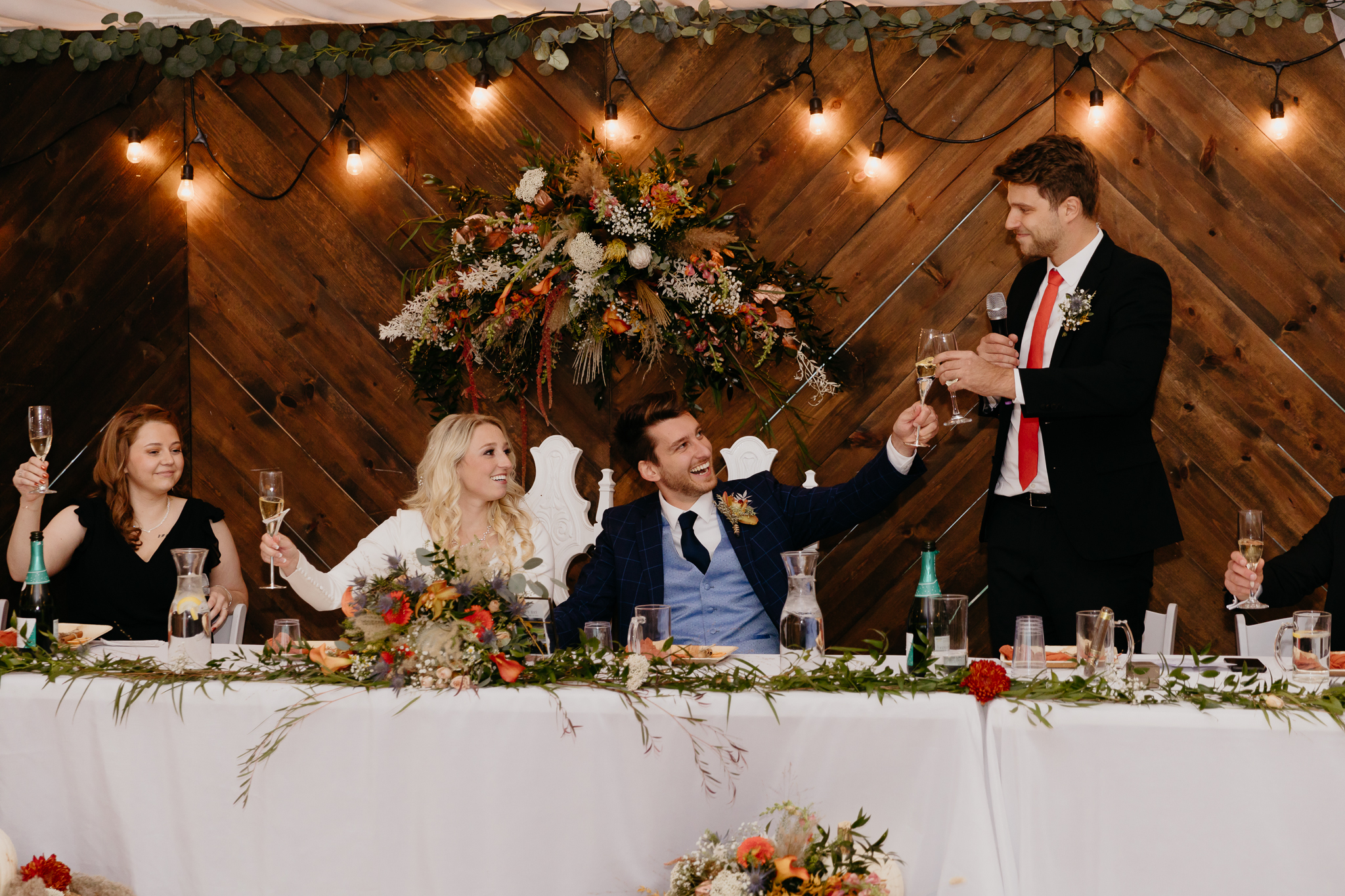 Groom and bride sitting at table, toast the best man after giving a speech in a white tent wedding