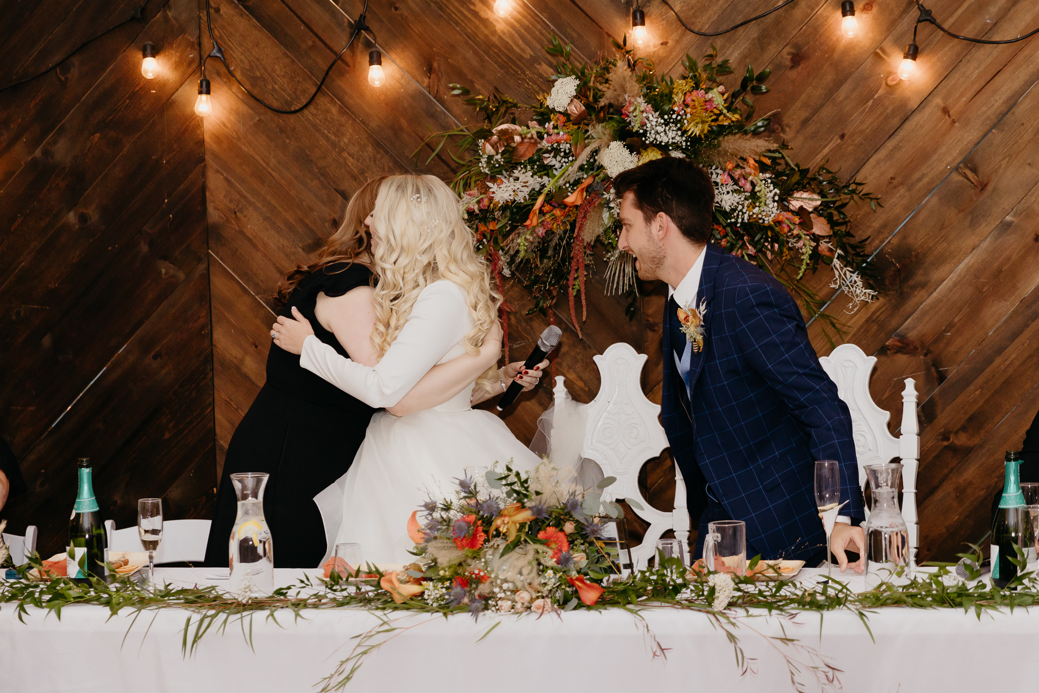 Groom and bride sitting at table, toast the maid of honor after giving a speech in a white tent wedding