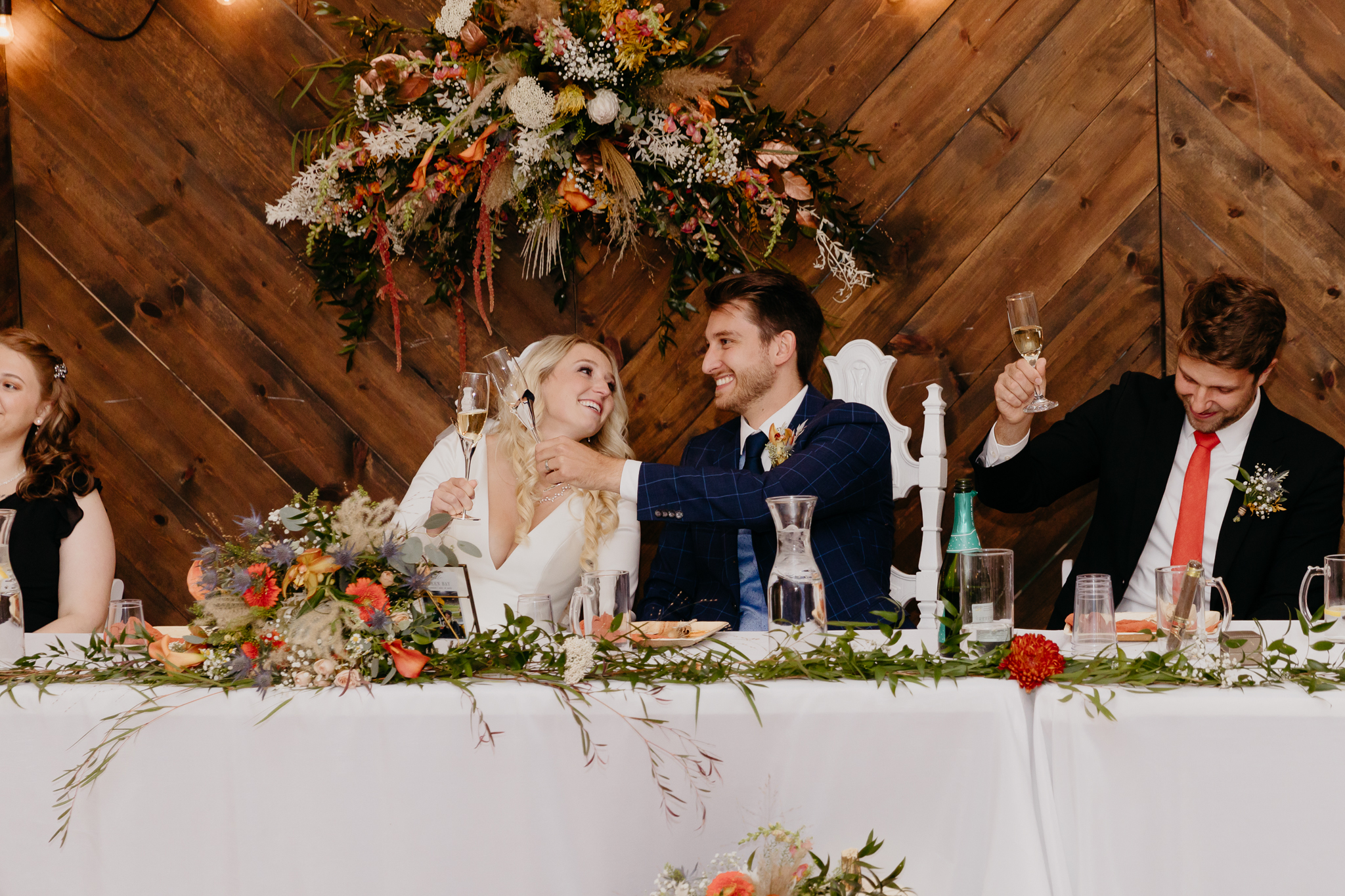 Bride and groom smile at each other at sitting at a table with flowers and food