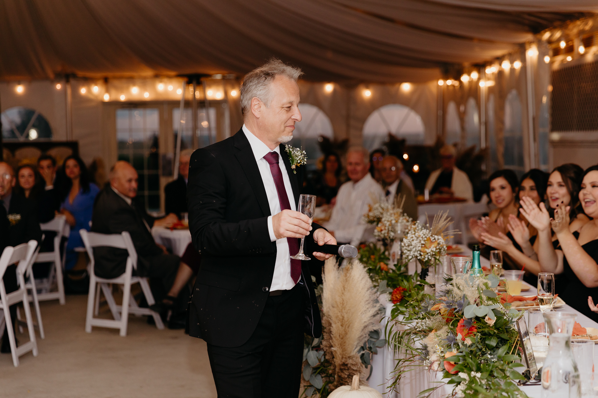 Father of the groom gives speech standing at white tent wedding