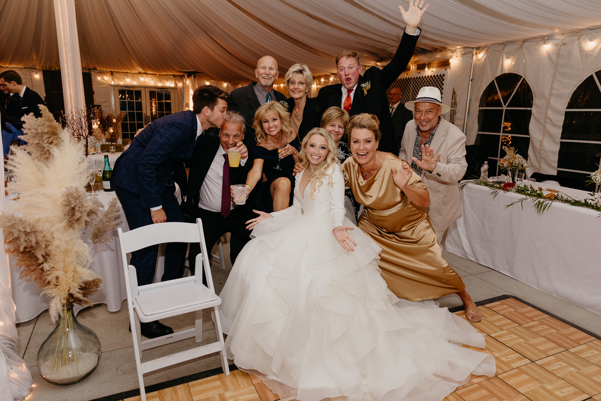 Bride and groom pose and smile with family and friends in a white tent wedding