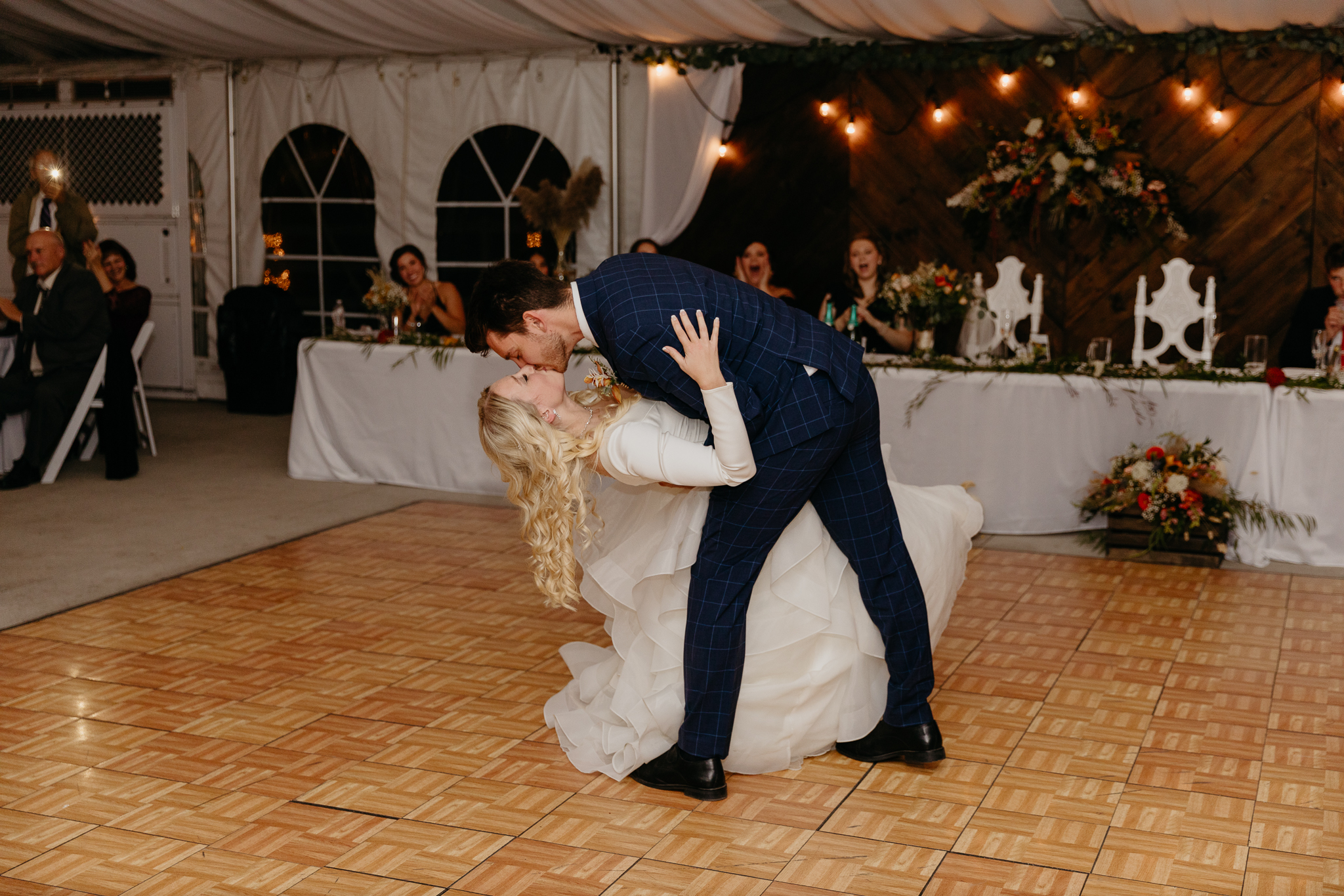 Bride and groom dancing together and kiss during their first dance, in a white tent wedding