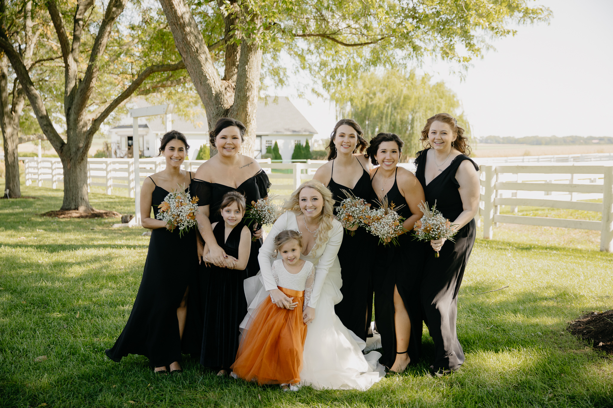 Bridesmaids and bride smile and laugh together with bouquets, standing in front of horse pastures at Northfork Farm