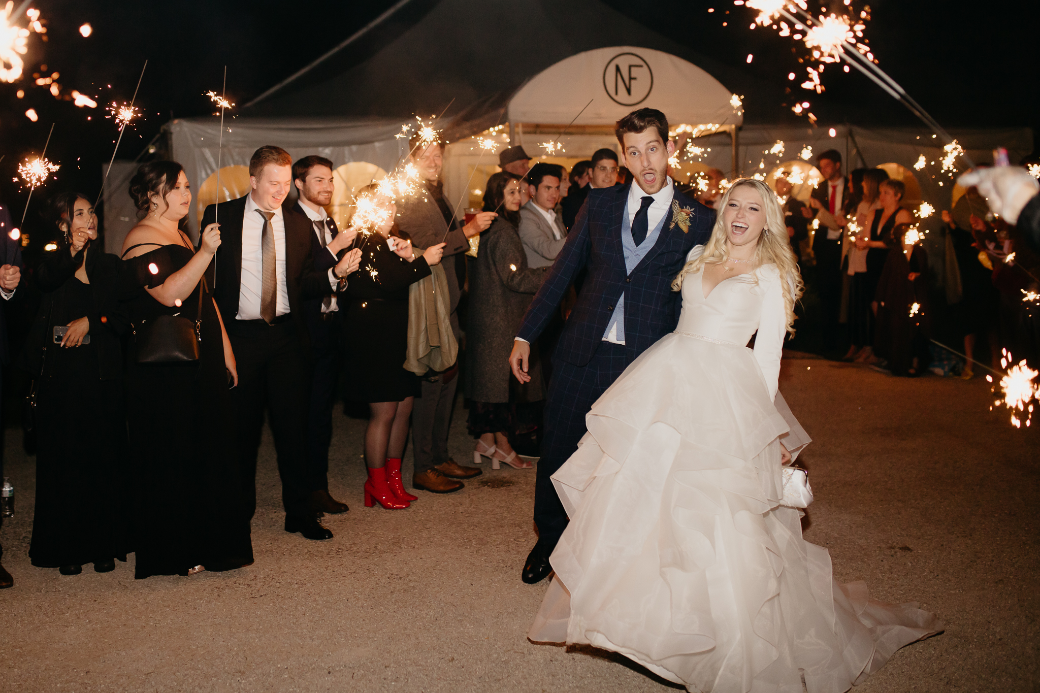 Bride and groom hold hands and run through sparklers and wedding guests at the end of their Northfork Farm Wedding