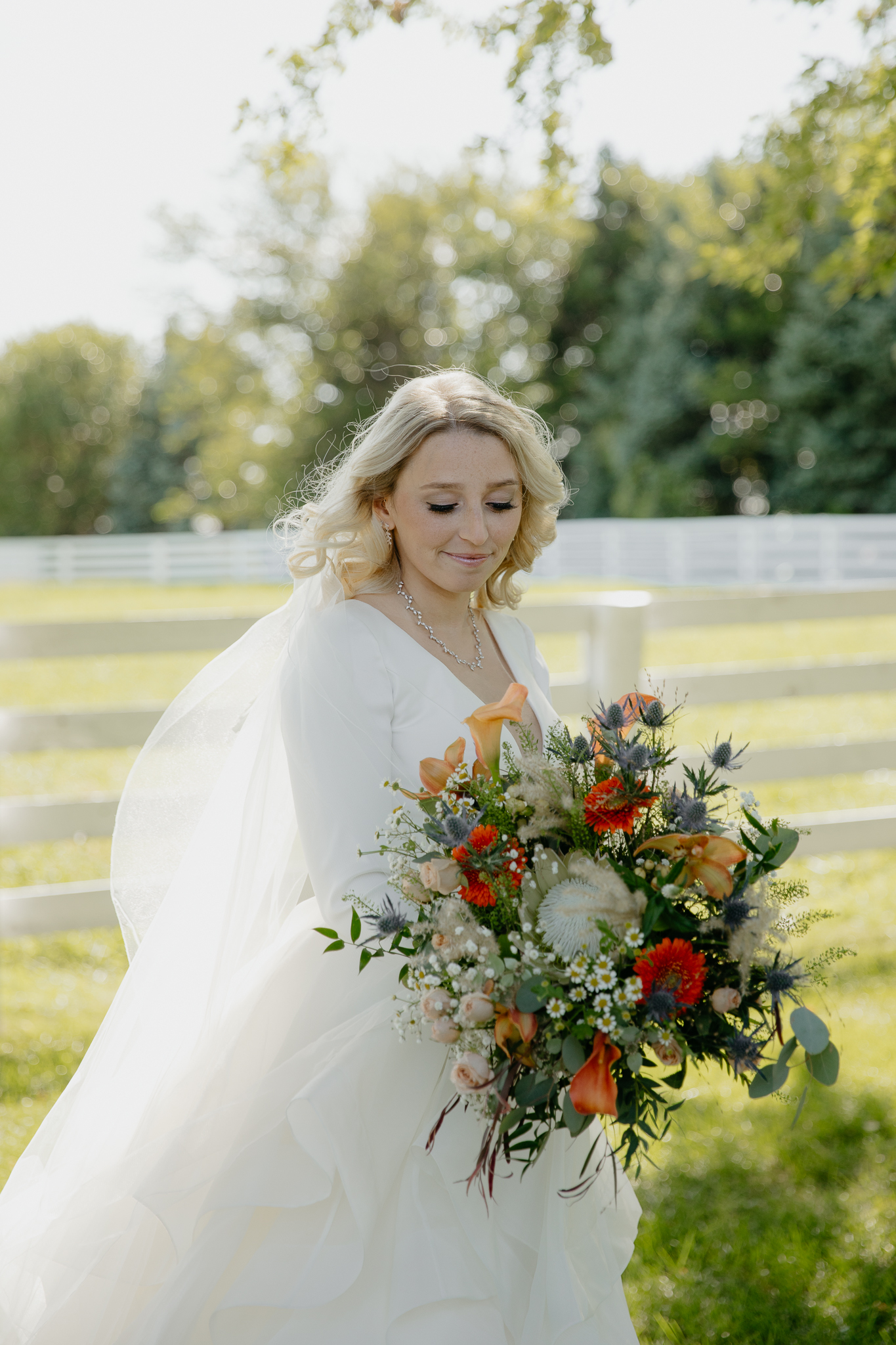 Portraits of bride in her wedding dress, with bouquet of flowers, near a horse pasture