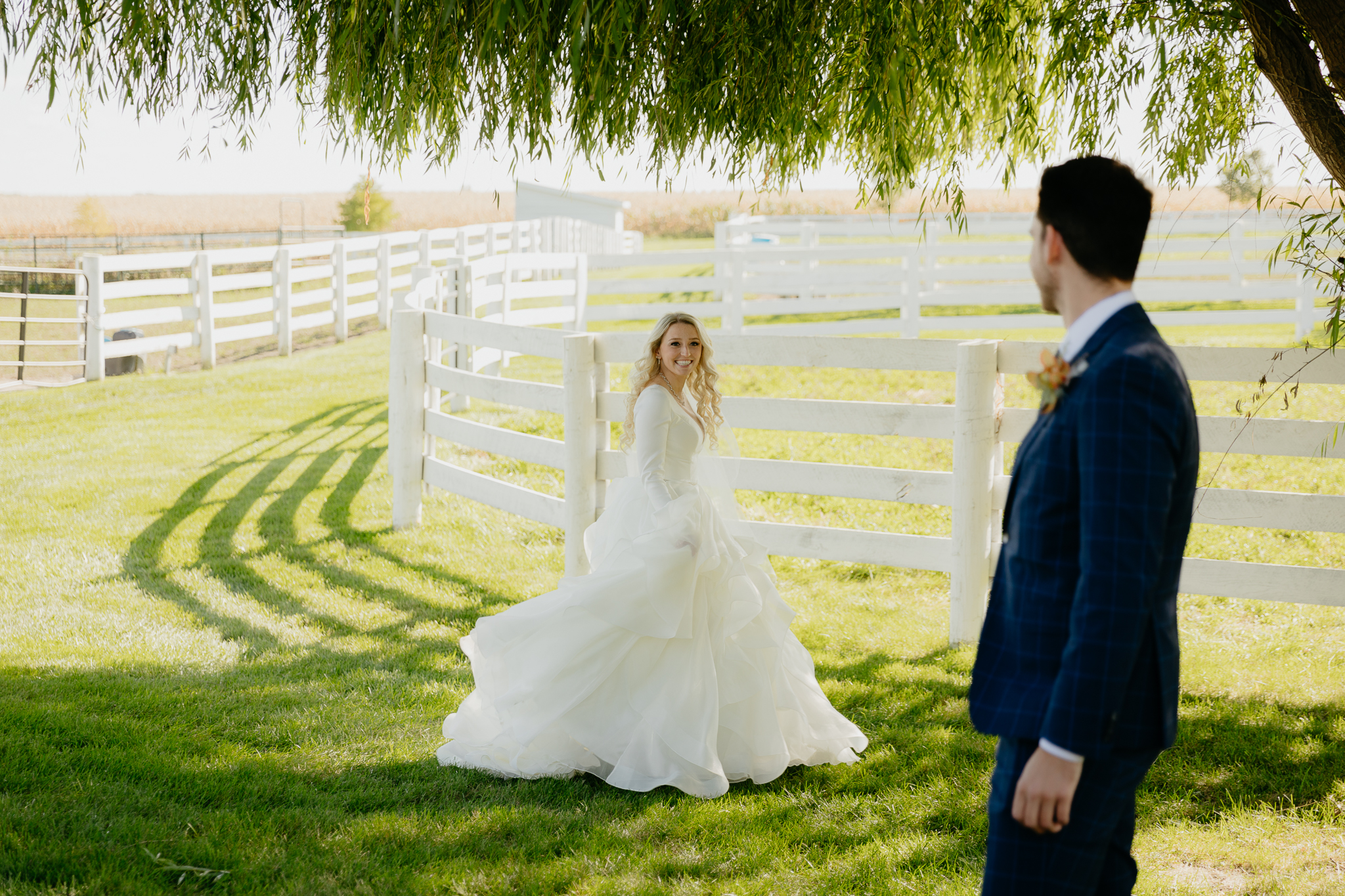 groom watches as his bride spins around underneath a willow tree, with horse pastures in the background