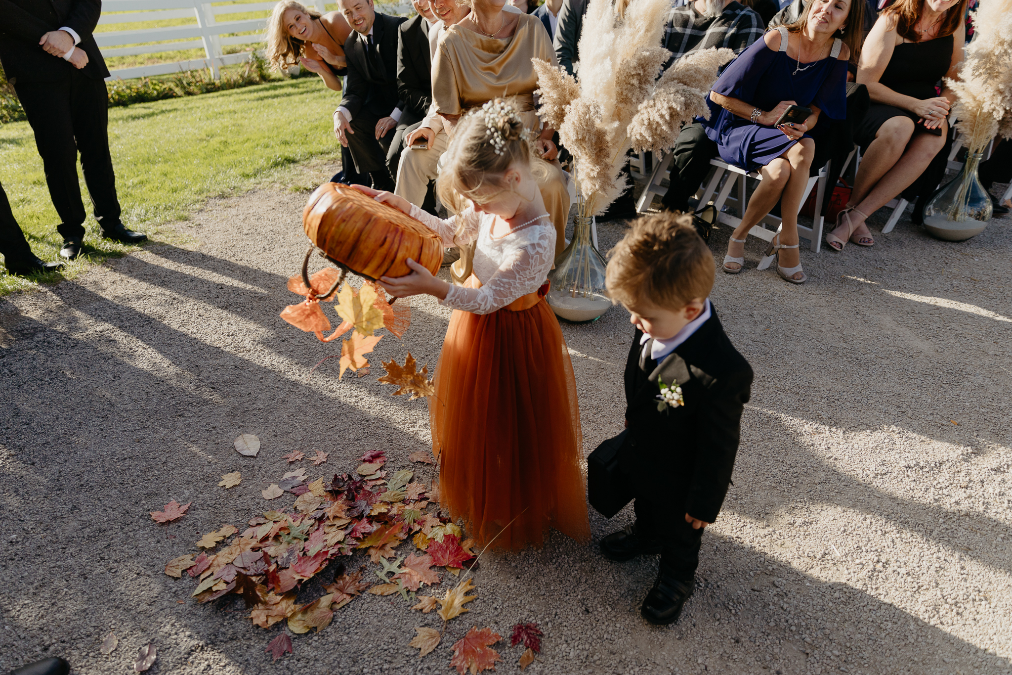 Flower girl dumps leaves on the ground at the wedding ceremony arch