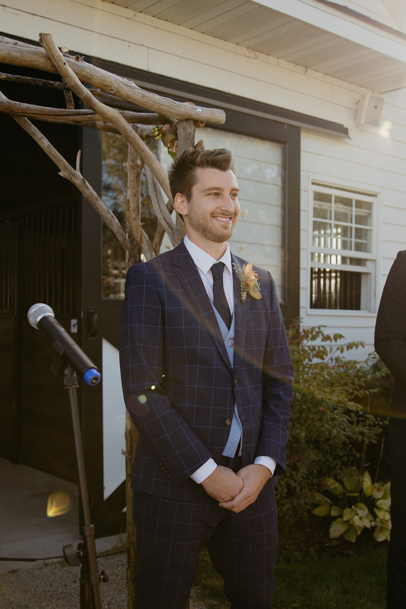 Groom smiles with barn behind him as his bride walks down the aisle
