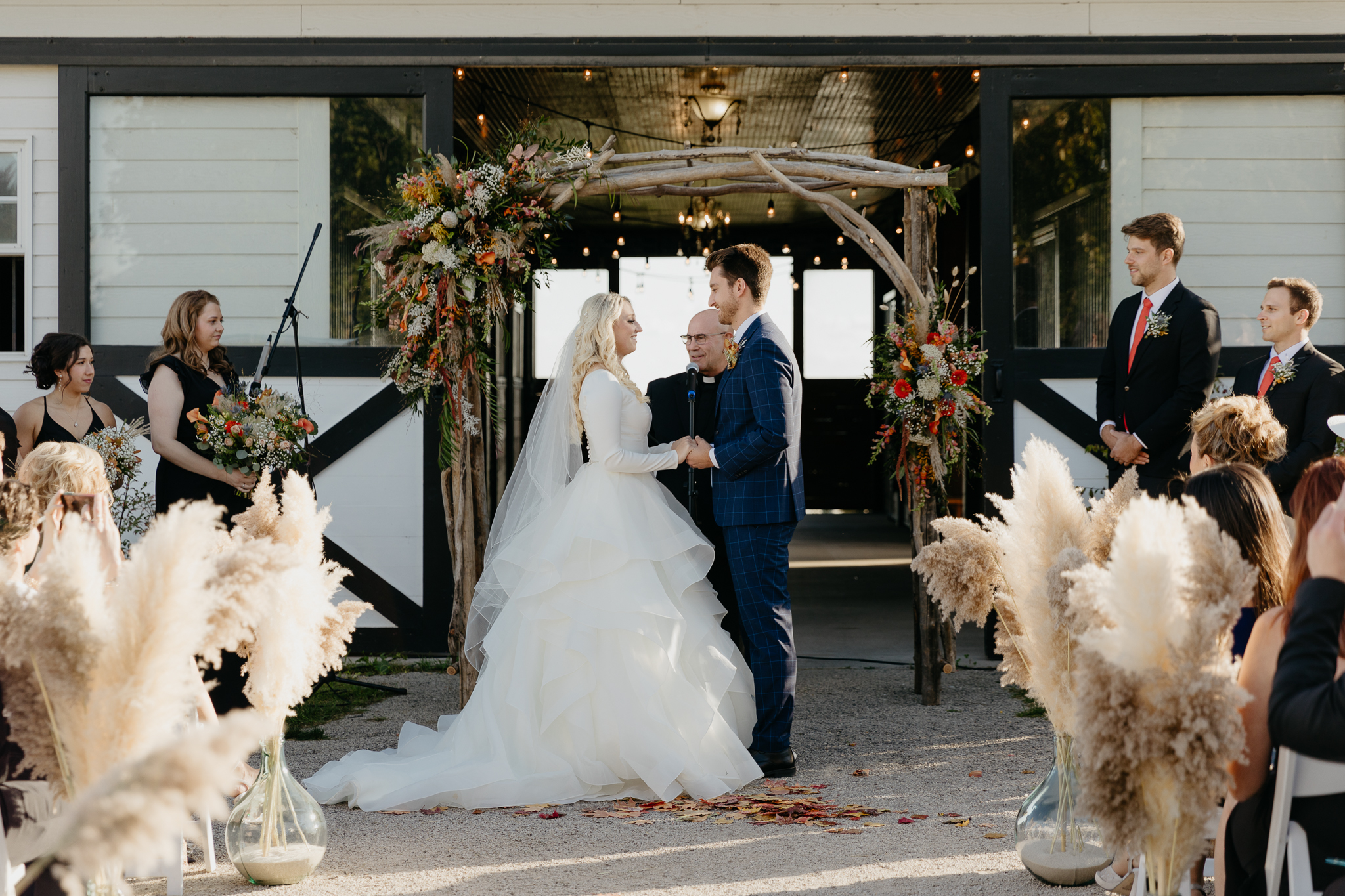 Bride and groom laugh and smile at each other while holding hands during their outdoor horse farm wedding in fall