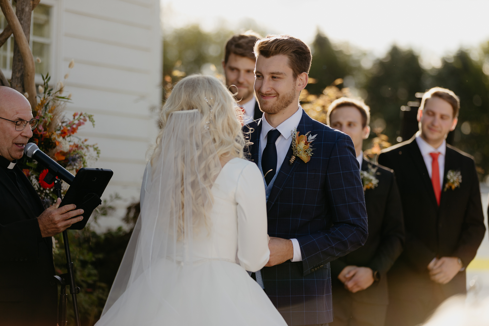 Groom smiling at his bride and holding his hands while exchanging vows at their outdoor wedding ceremony