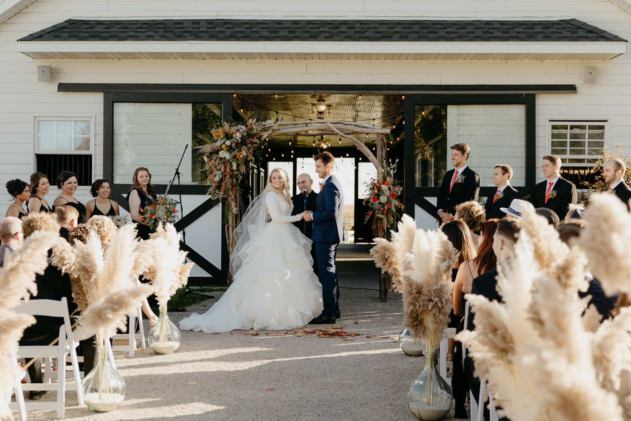 Bride and groom laugh and smile at each other while holding hands during their outdoor horse farm wedding in fall