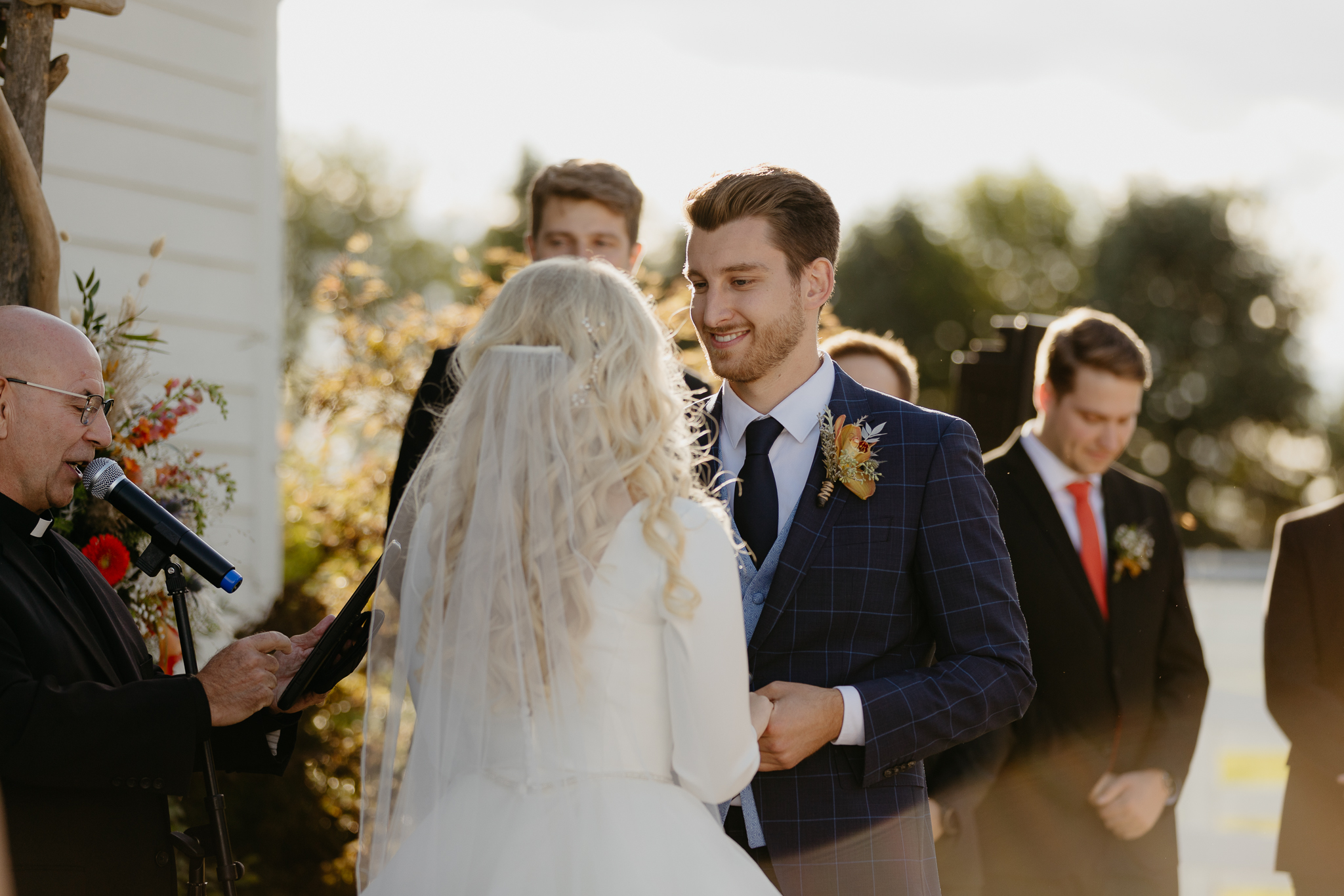 Groom smiling at his bride and holding his hands while exchanging vows at their outdoor wedding ceremony