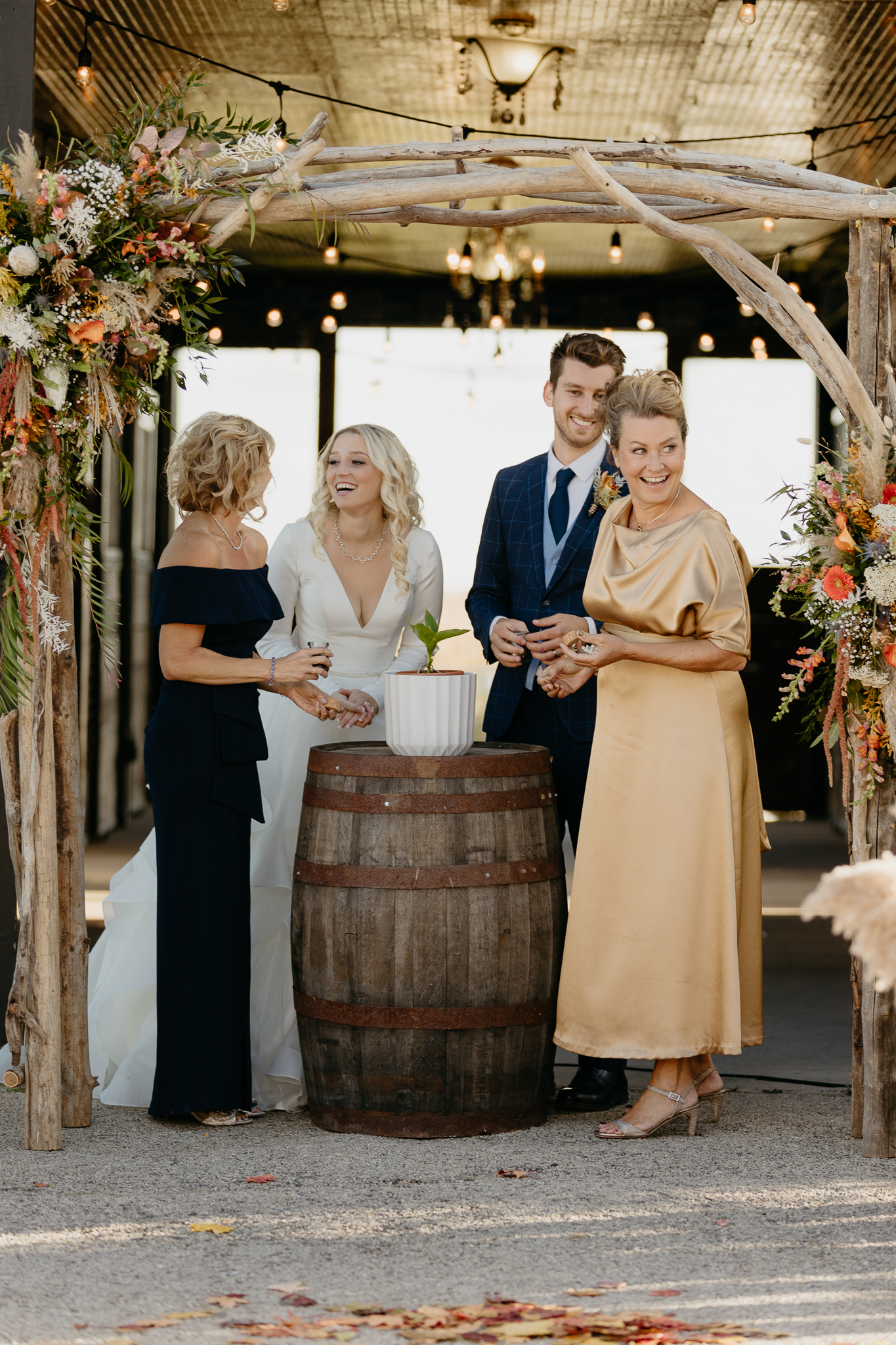 Bride, Groom, and mothers pour soil into a plant at the altar of an outdoor wedding ceremony