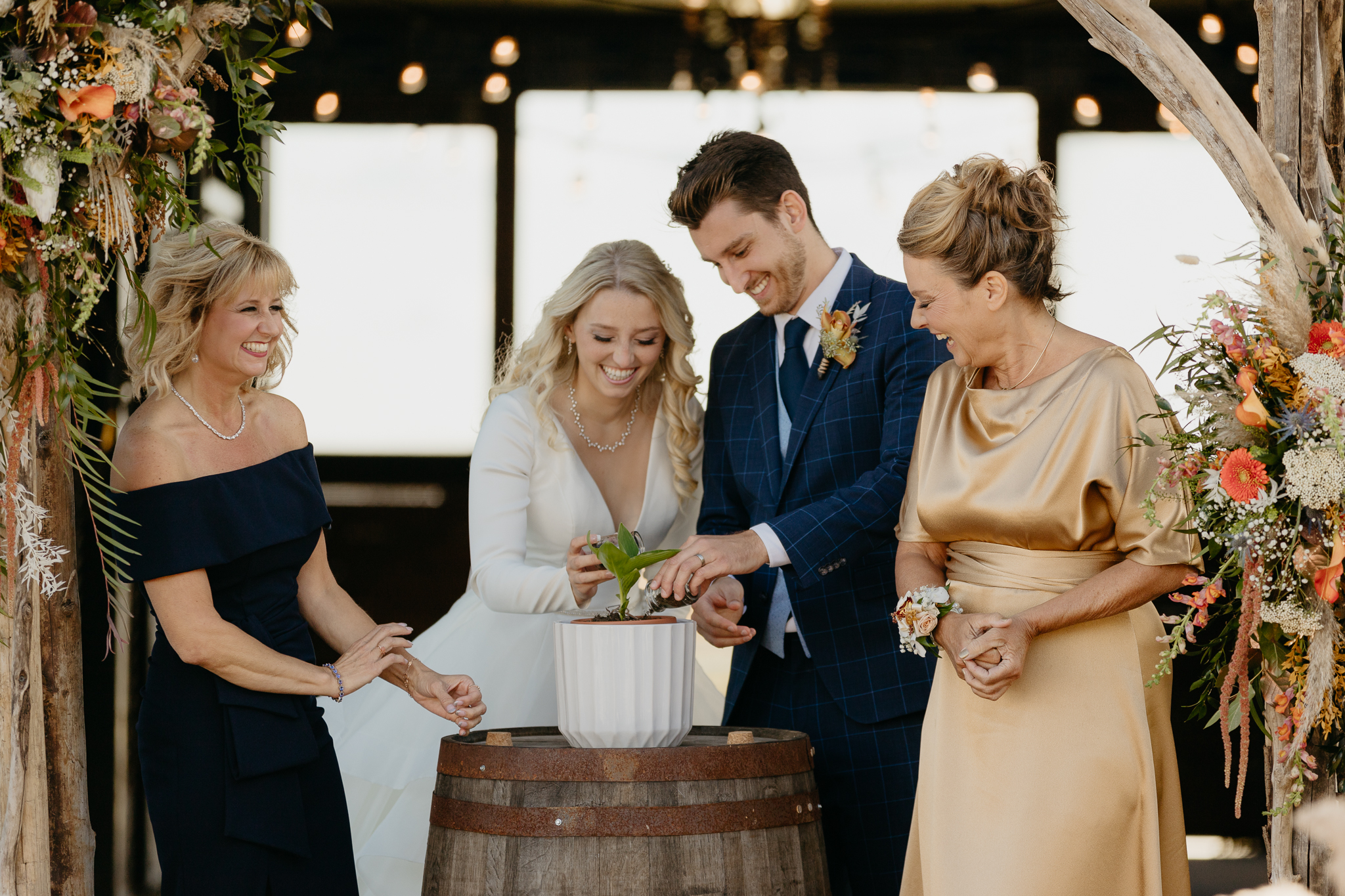 Bride, Groom, and mothers pour soil into a plant at the altar of an outdoor wedding ceremony