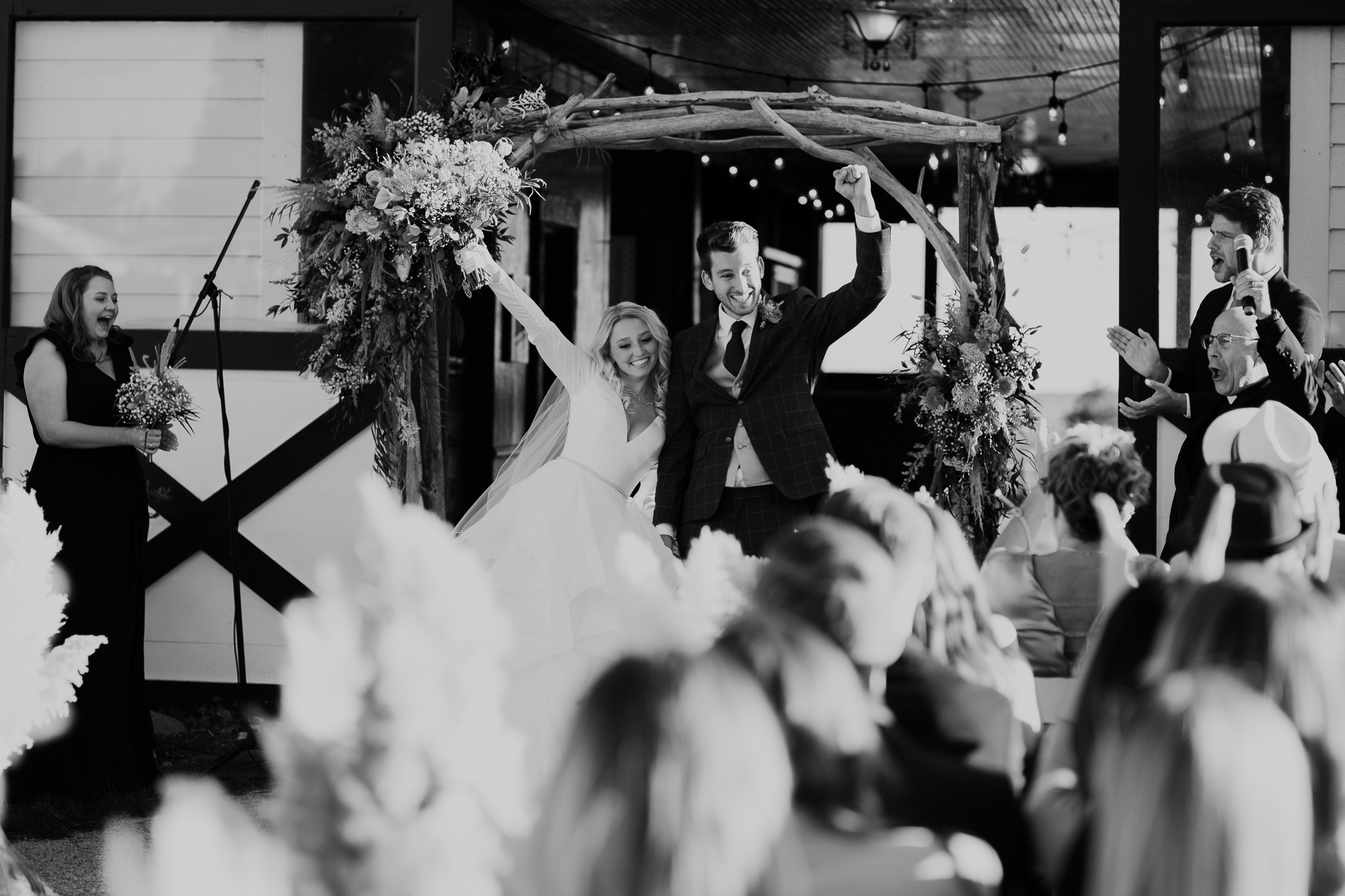 Bride and groom holding hands in air to celebrate being newly married, walk back down the aisle of their outdoor wedding