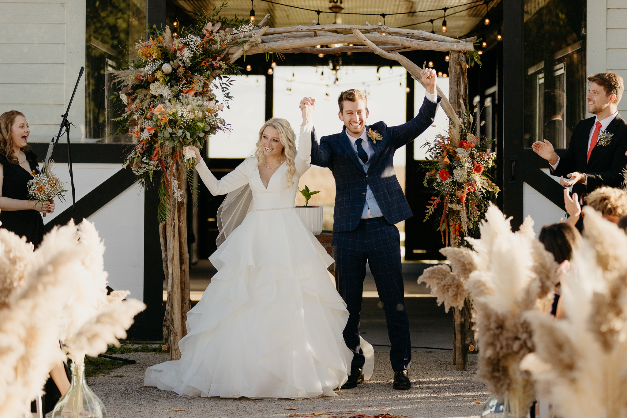 Bride and groom holding hands in air to celebrate being newly married, walk back down the aisle of their outdoor wedding