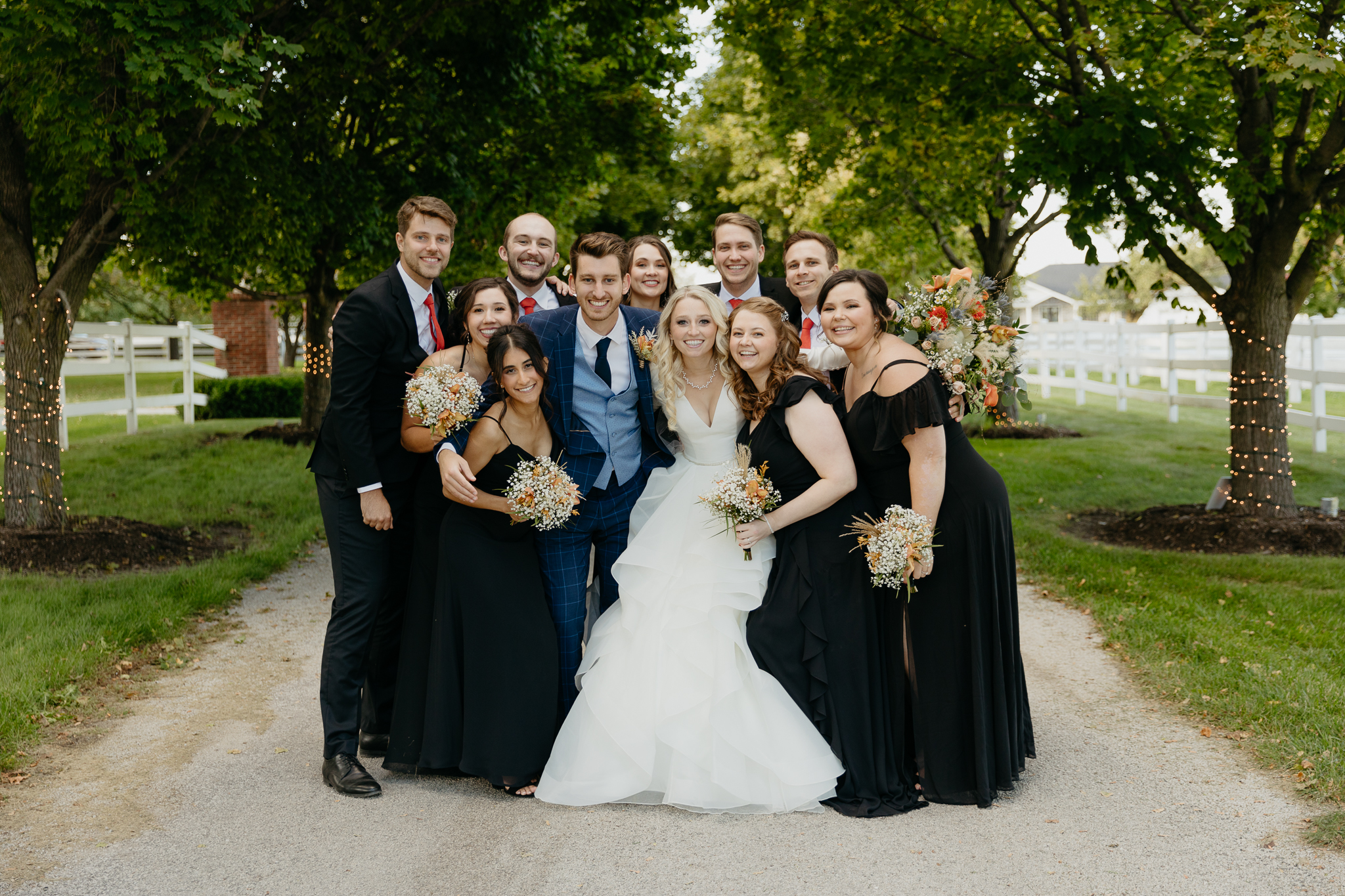 Wedding party of bridesmaids and groomsmen cheer as groom and bride kiss in a tree lined driveway at Northfork Farm