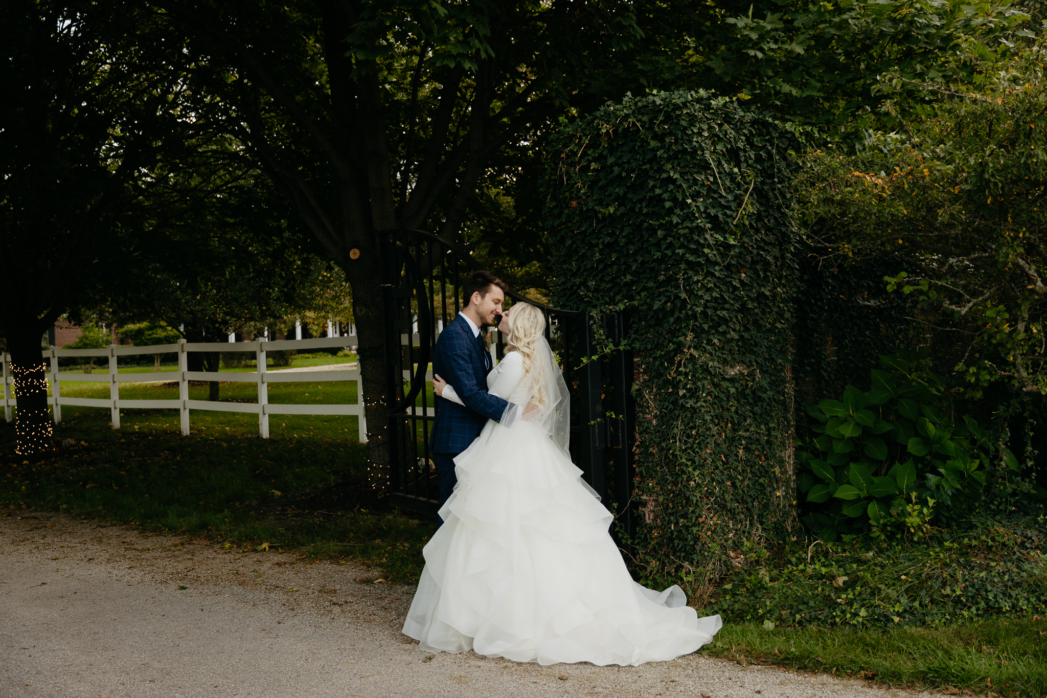 Bride and groom kiss and embrace next to an ivy covered wrought iron gate