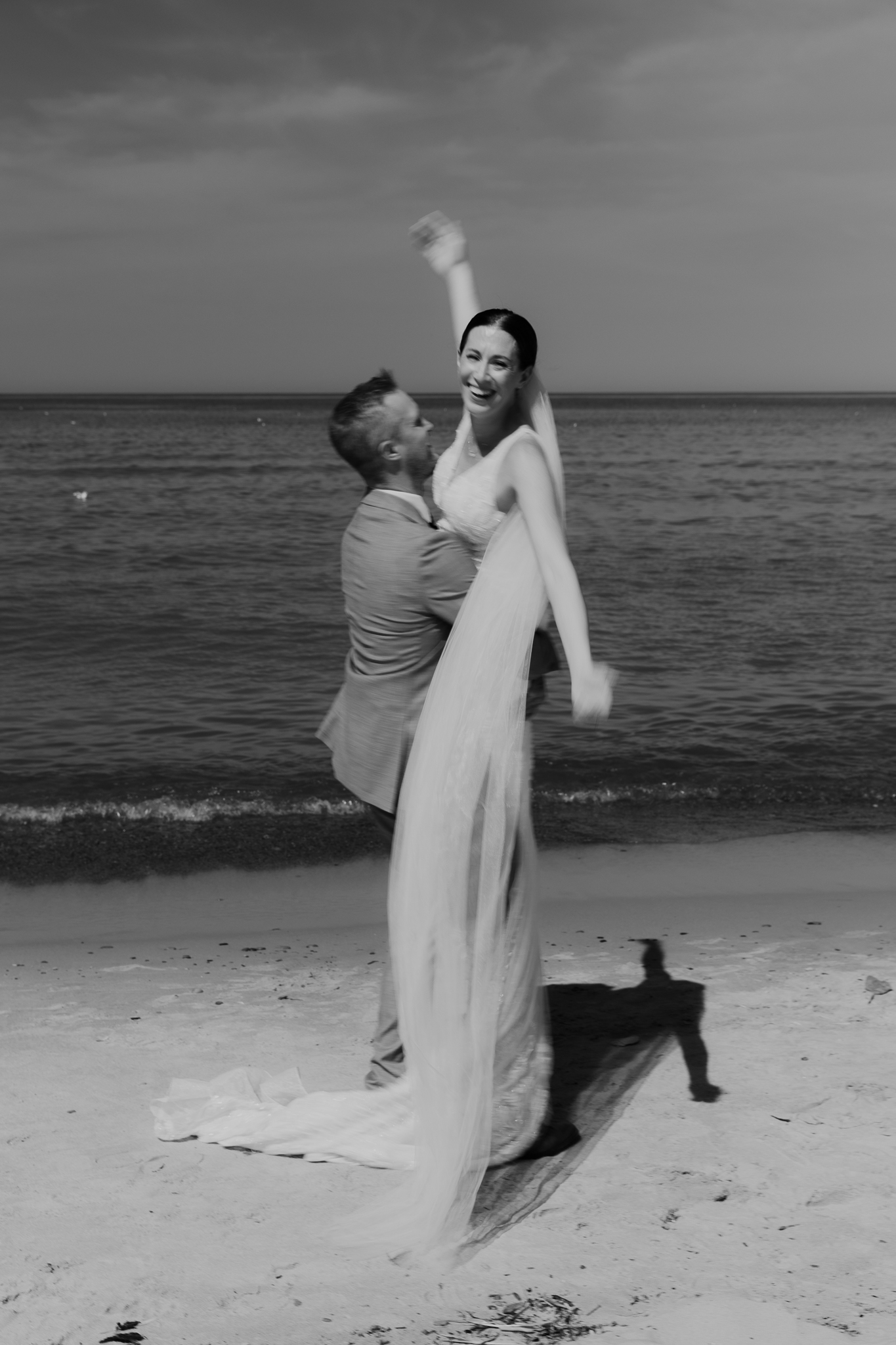 Groom lifts bride in the air and spins her around during their Lake Michigan beach elopement