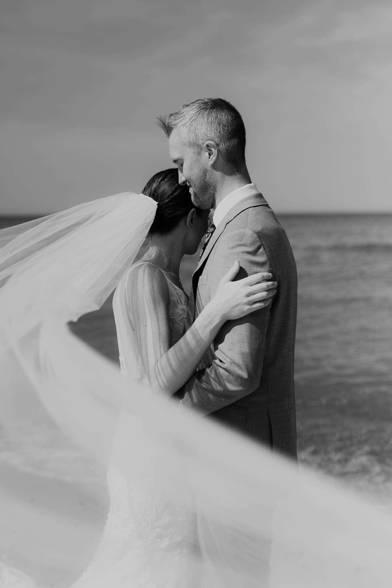 Bride and groom embrace while taking couple photos along the beach at their Warren Dunes State Park elopement