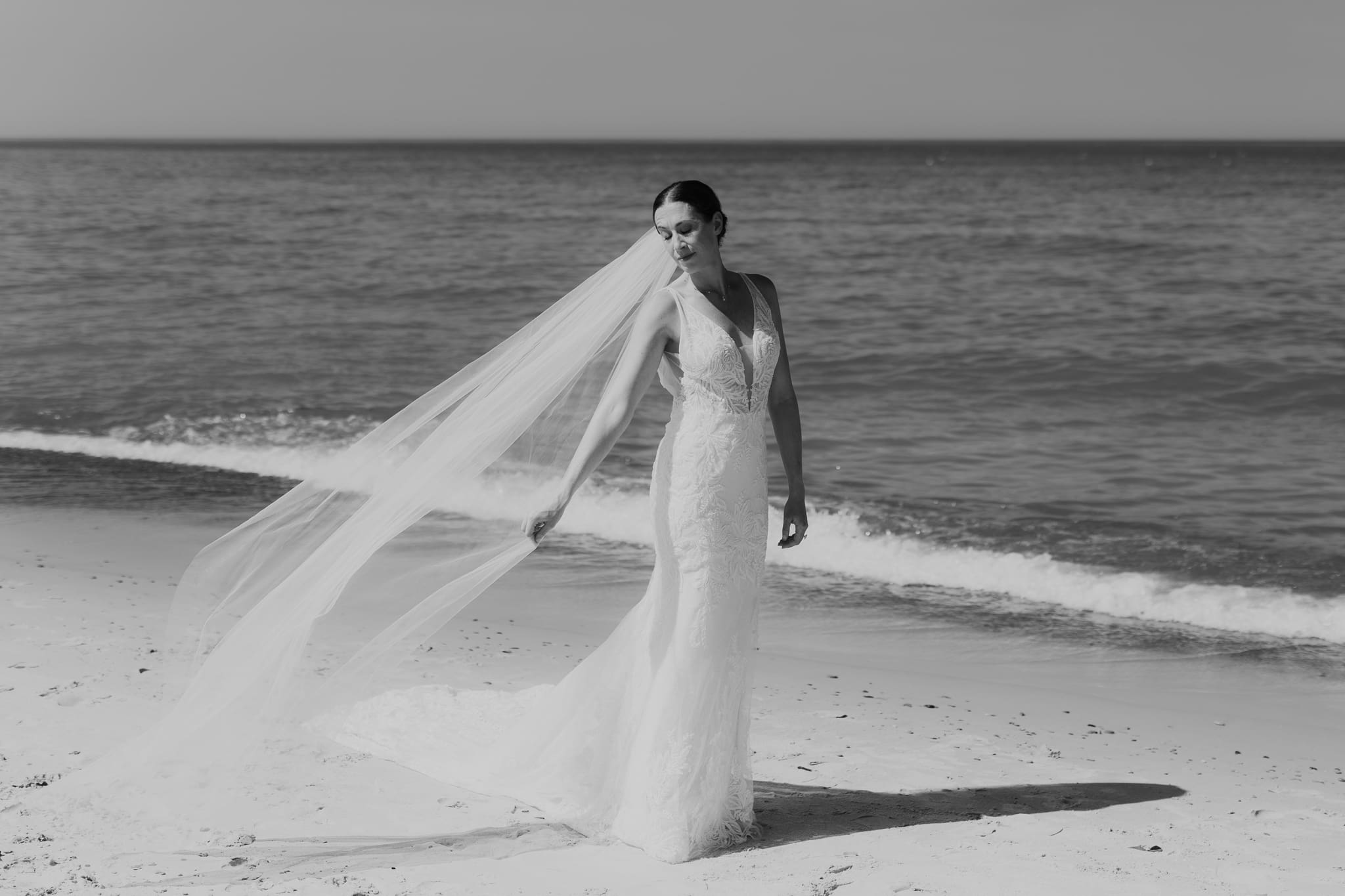 Bride poses next to the shoreline of Lake Michigan with her wedding veil blowing in the wind 