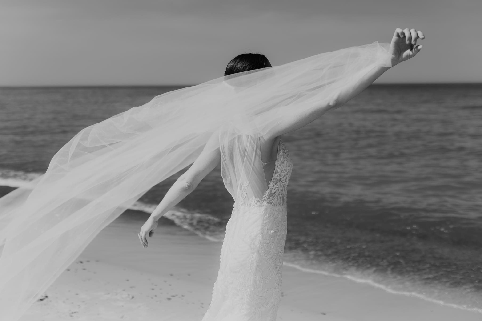 Bride poses next to the shoreline of Lake Michigan with her wedding veil blowing in the wind 