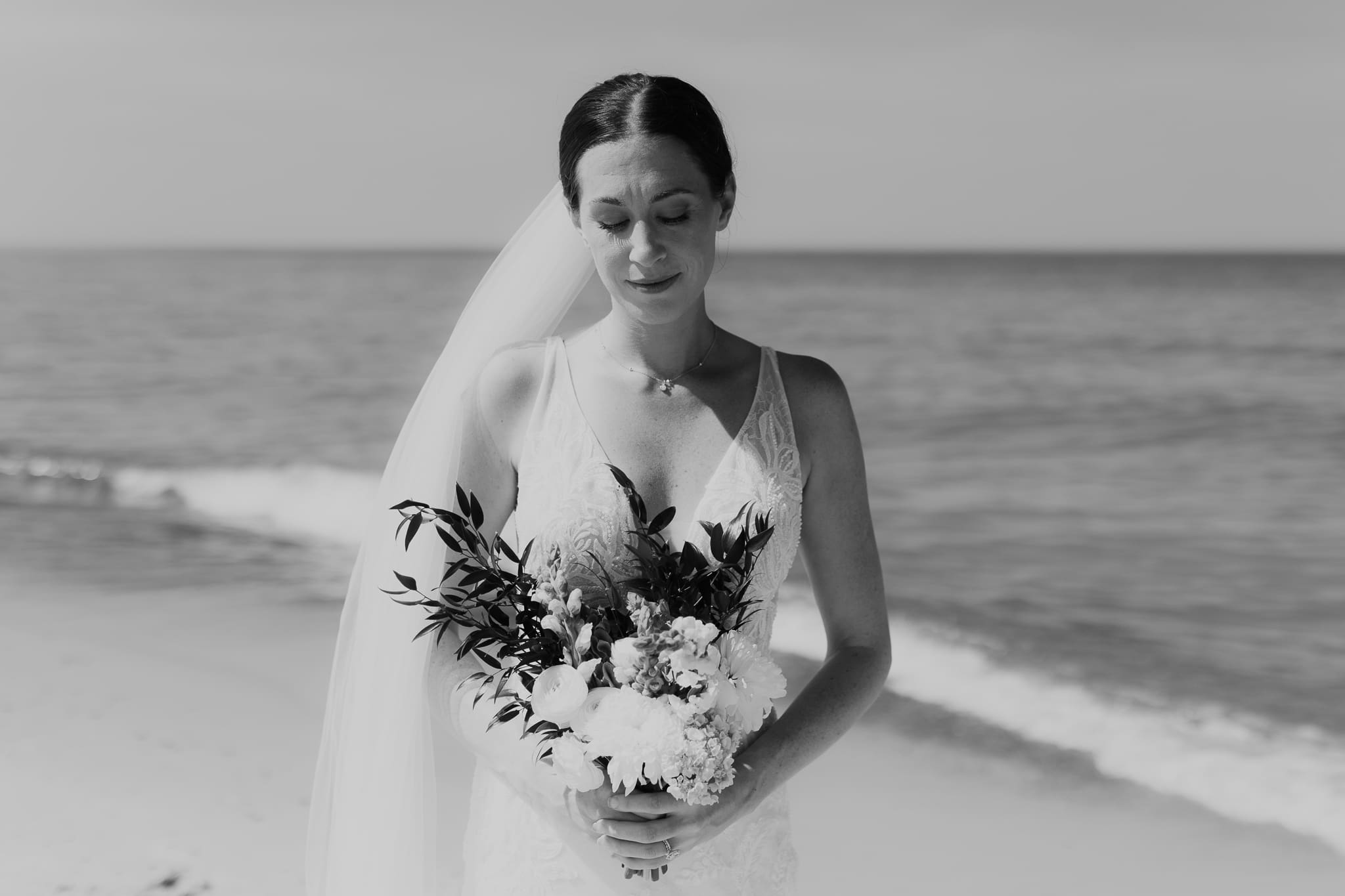 Bride poses next to the shoreline of Lake Michigan with her wedding veil blowing in the wind 