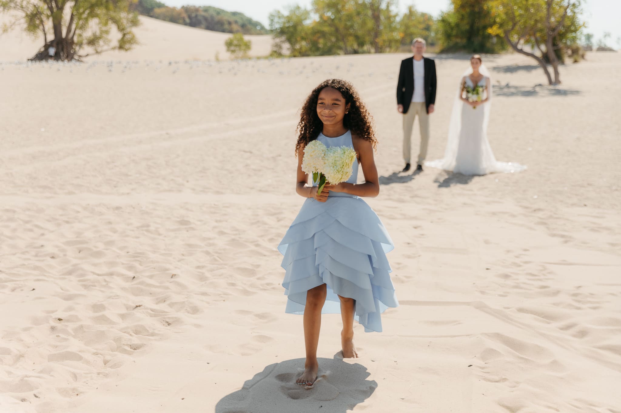 Flower girl walks down the aisle during a sunny beach wedding at Warren Dunes State Park