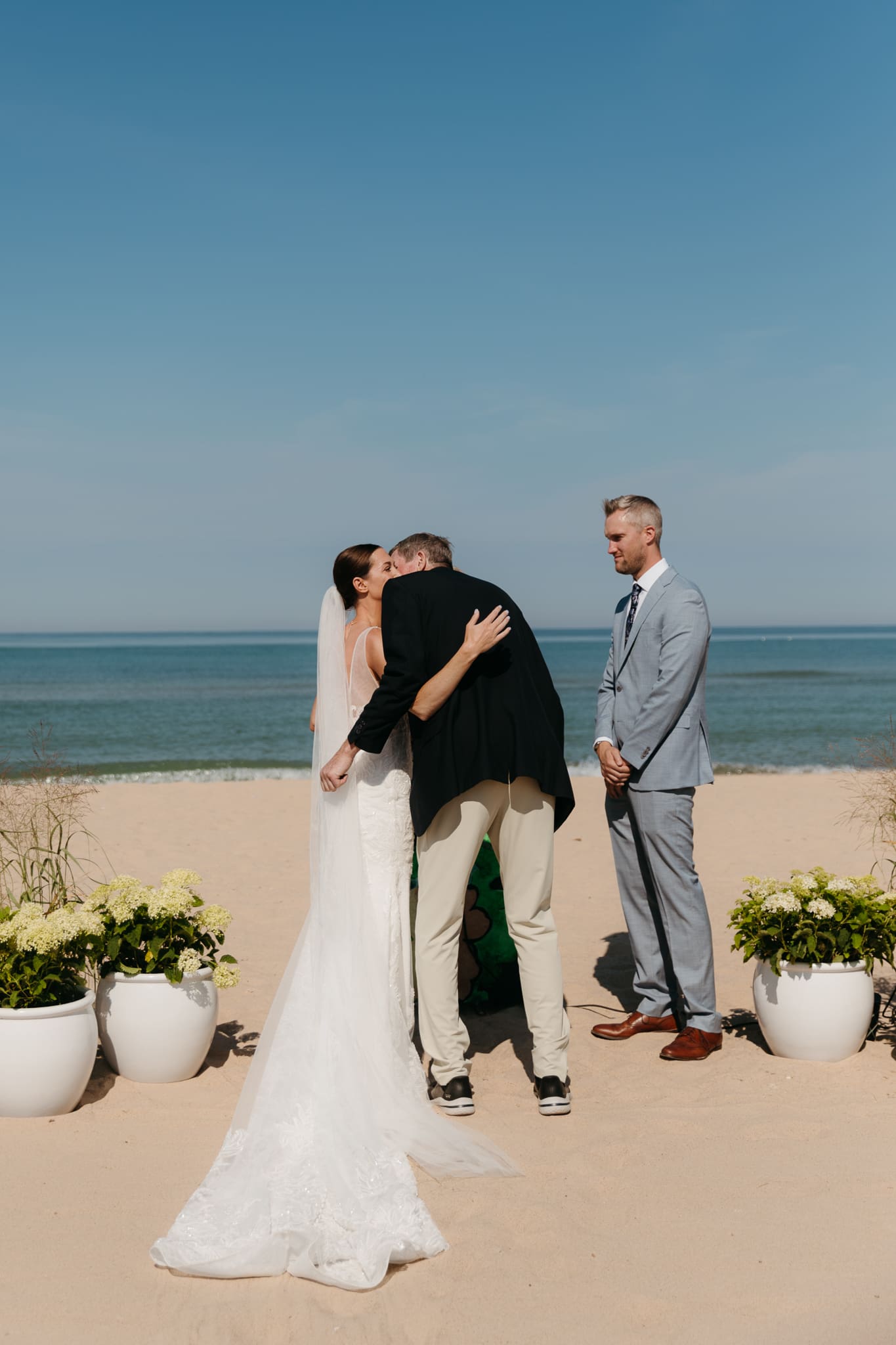 Bride and groom hug father before starting their beach wedding ceremony on Lake Michigan