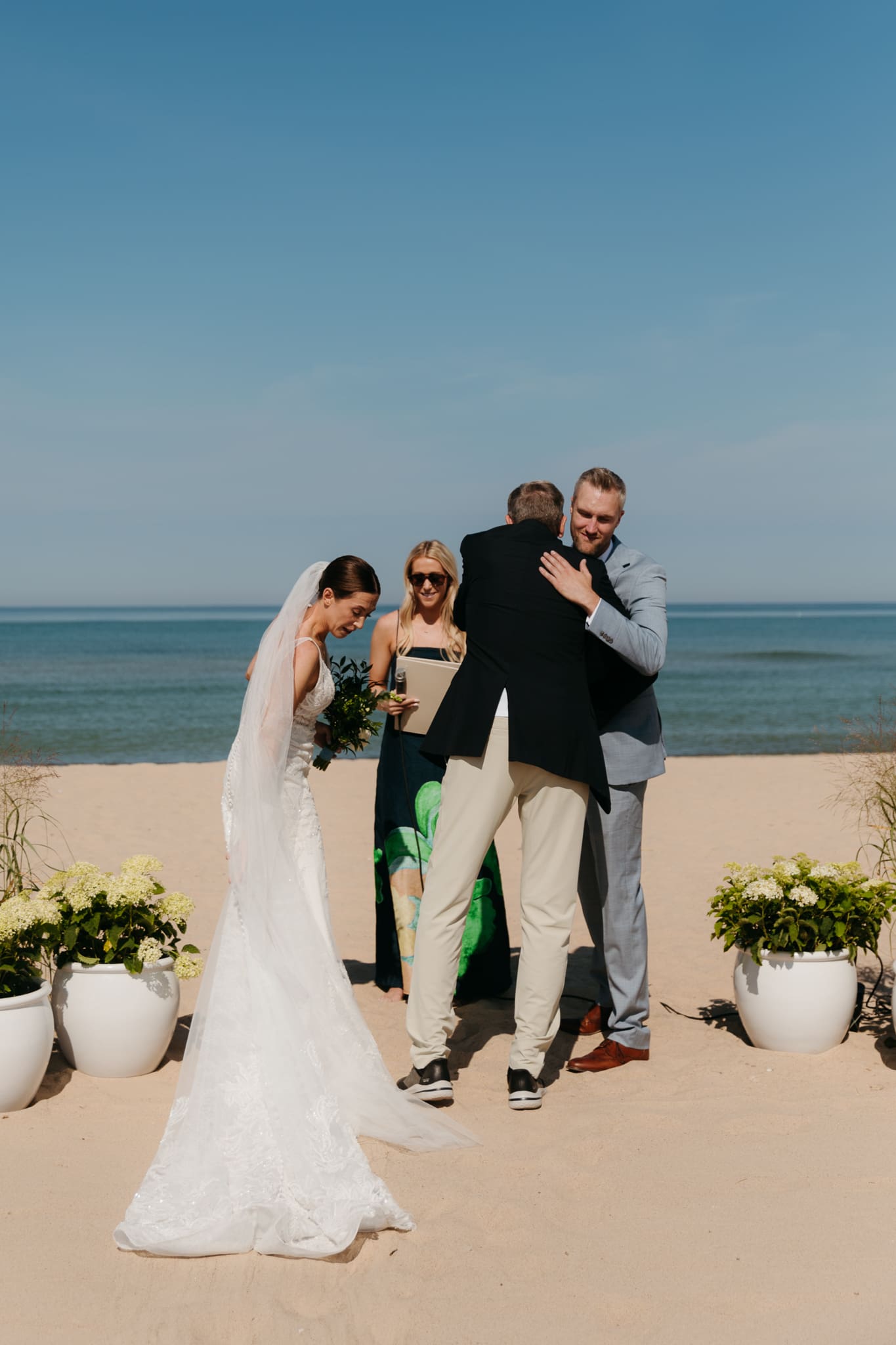 Bride and groom hug father before starting their beach wedding ceremony on Lake Michigan