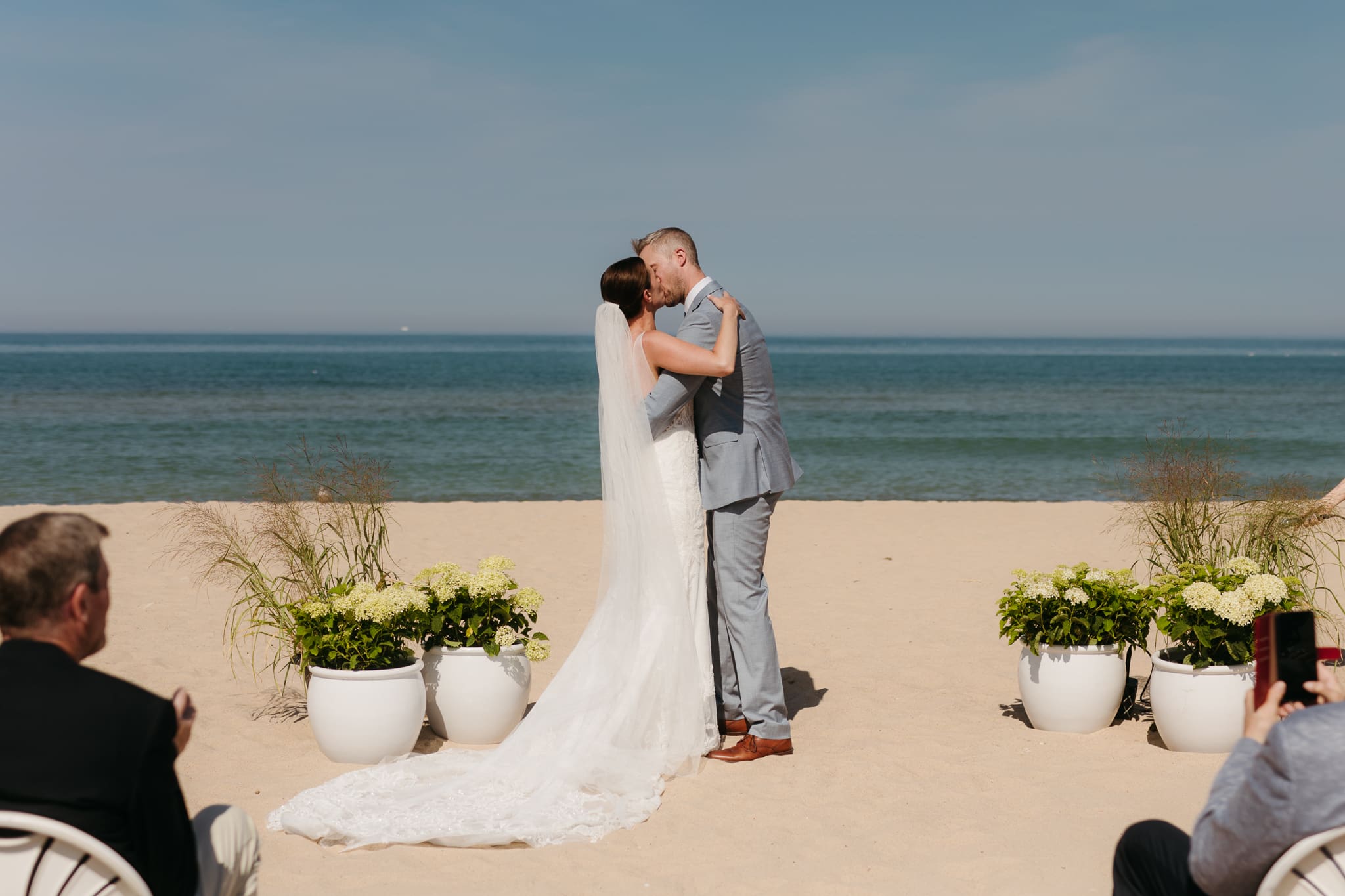 Bride and groom exchange vows and rings then share a first kiss on the beach during their Lake Michigan wedding ceremony at Warren Dunes State Park