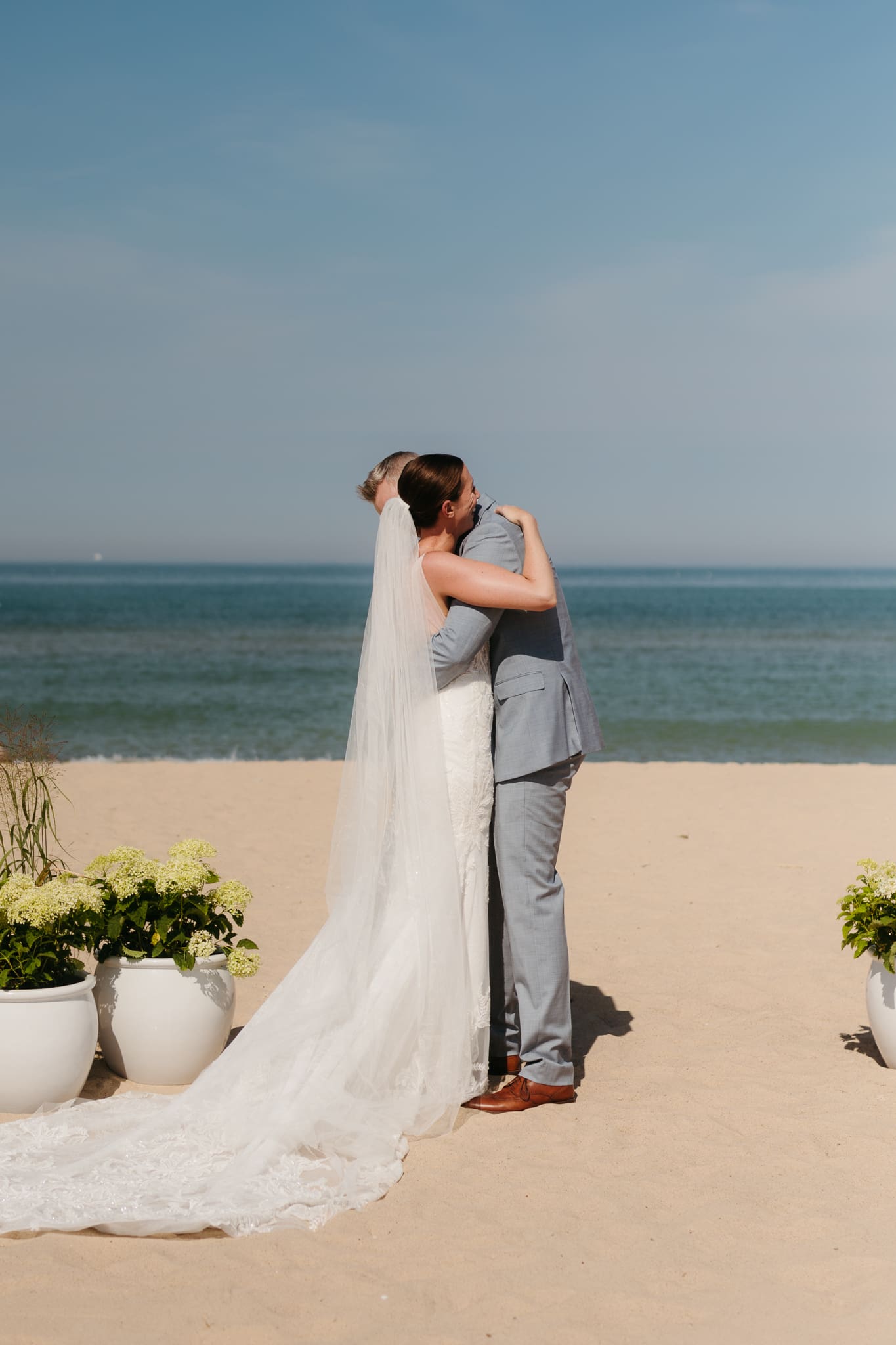 Bride and groom embrace in a hug after sealing their wedding ceremony with a first kiss, during their Lake Michigan beach wedding