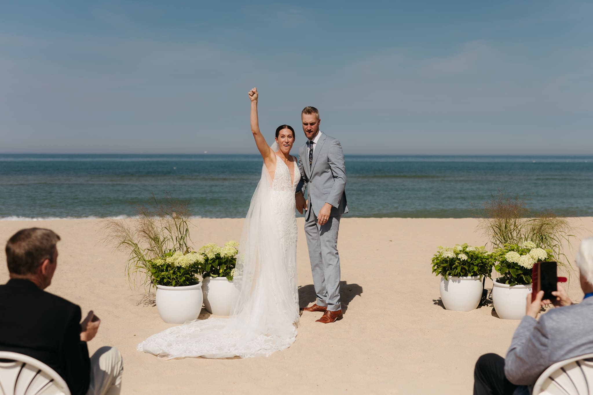 Bride and groom embrace and celebrate after sealing their wedding ceremony with a first kiss, during their Lake Michigan beach wedding