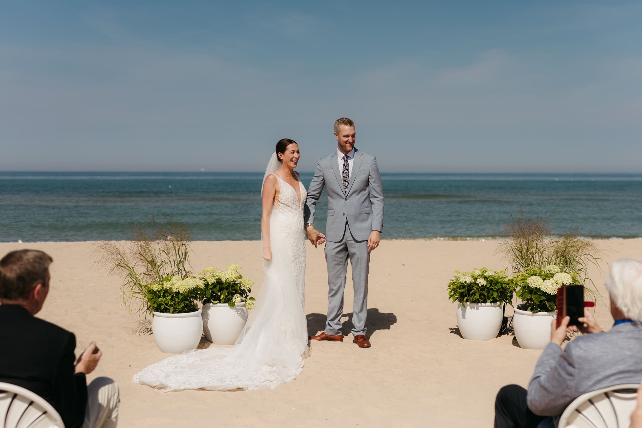 Bride and groom embrace and celebrate after sealing their wedding ceremony with a first kiss, during their Lake Michigan beach wedding
