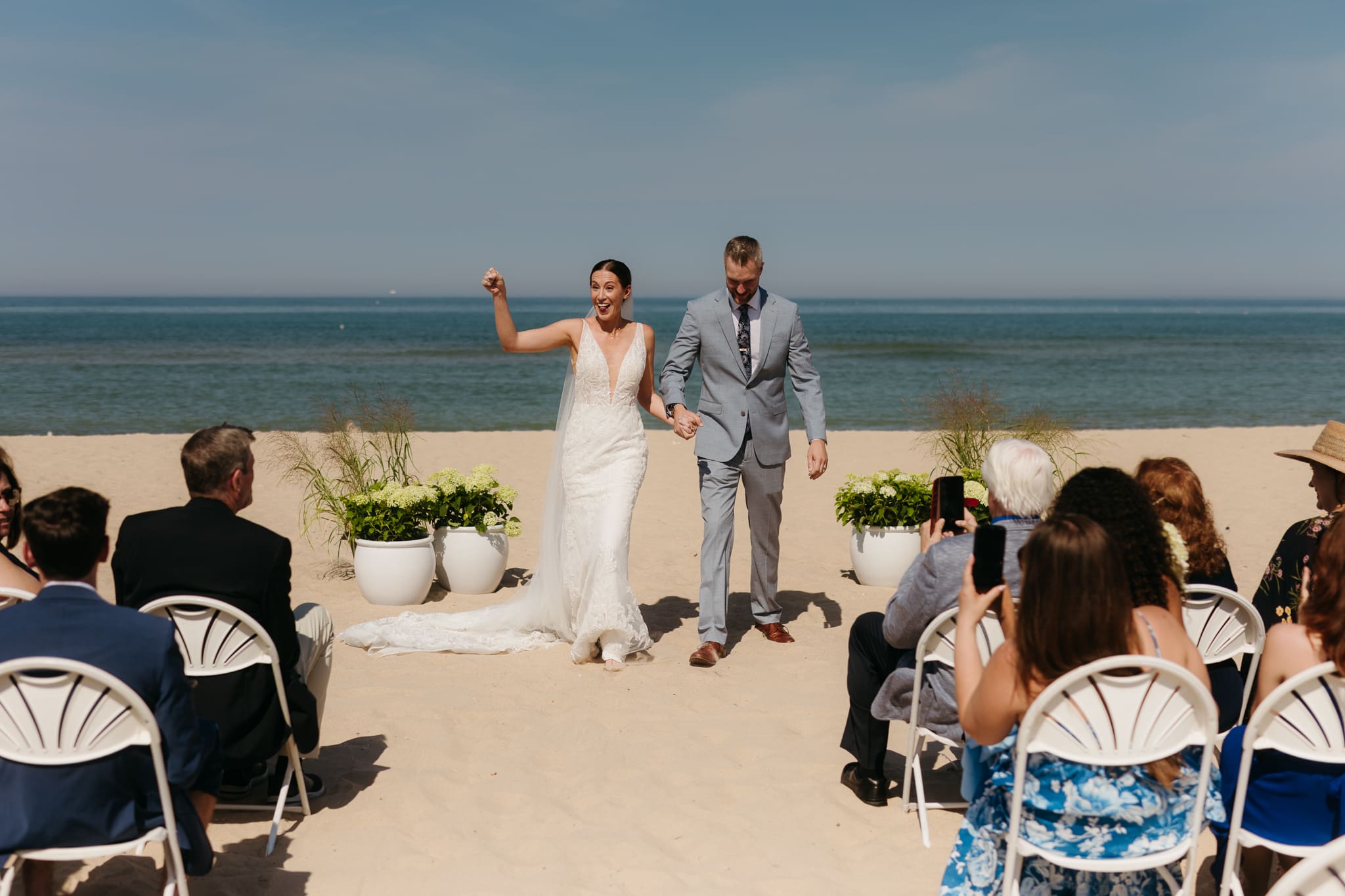 Bride and groom embrace and celebrate after sealing their wedding ceremony with a first kiss, during their Lake Michigan beach wedding