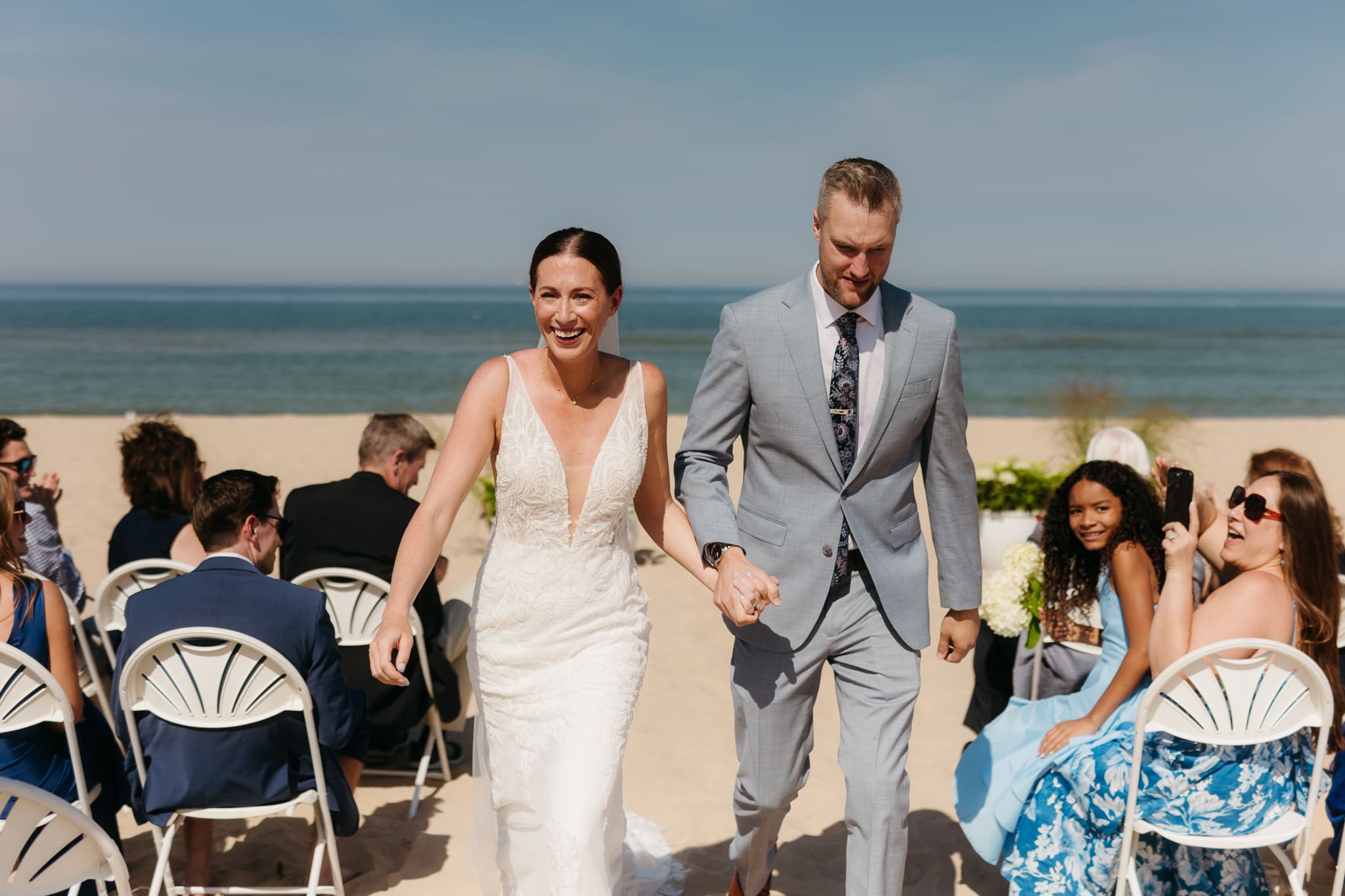 Bride and groom embrace and celebrate after sealing their wedding ceremony with a first kiss, during their Lake Michigan beach wedding