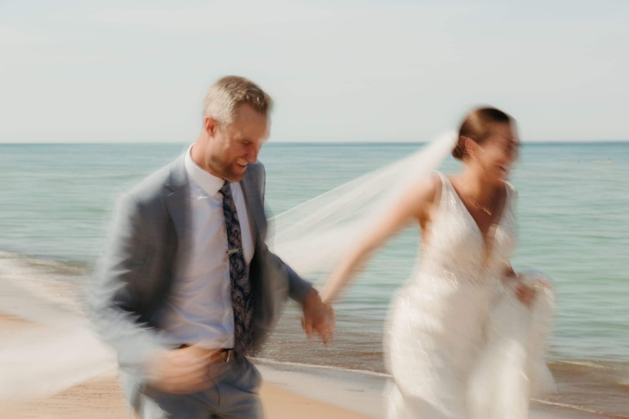 Bride and groom embracing and enjoying their Warren Dunes State Park elopement while running along the beach