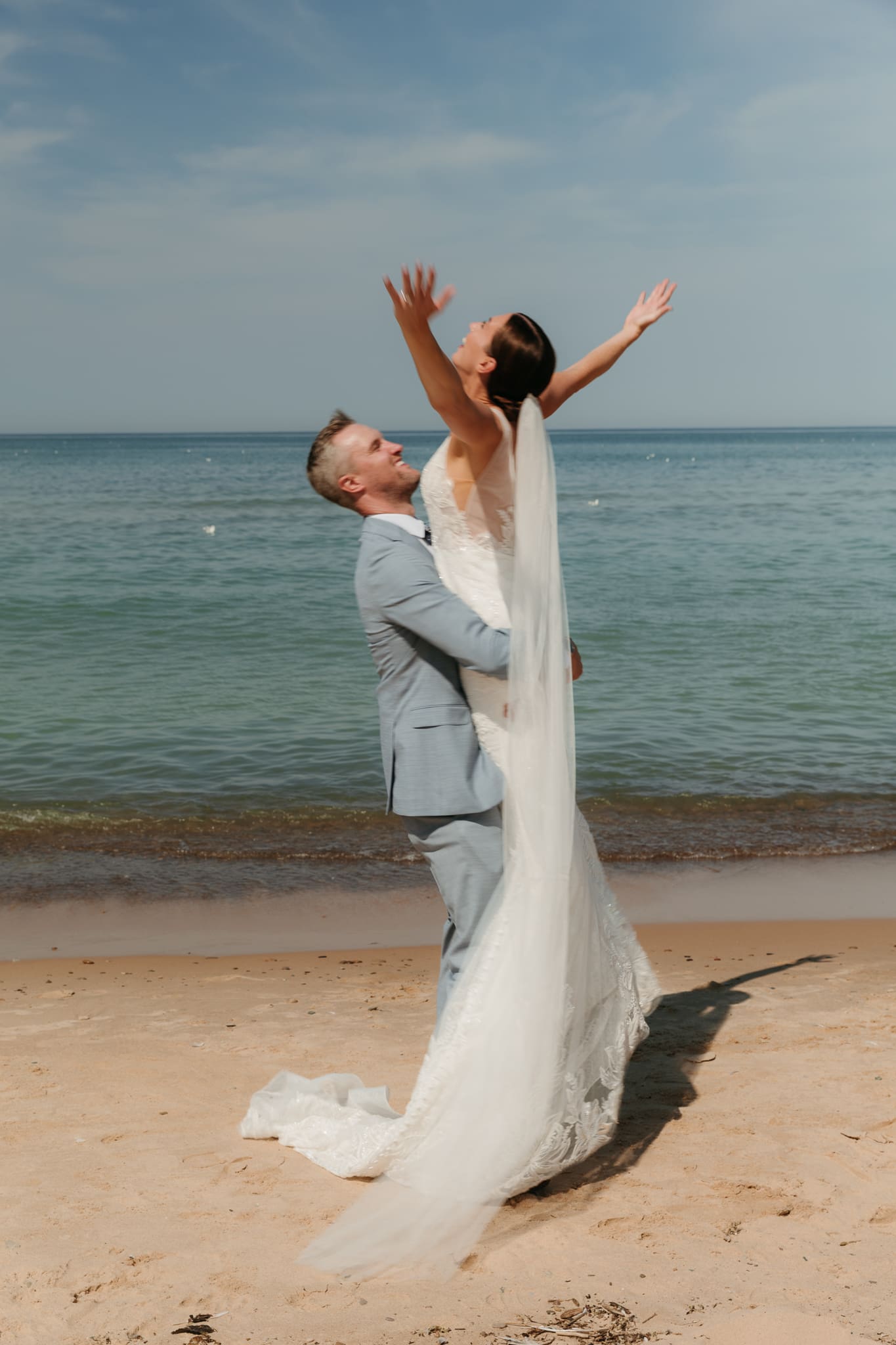 Groom lifts bride in the air and spins her around during their Lake Michigan beach elopement