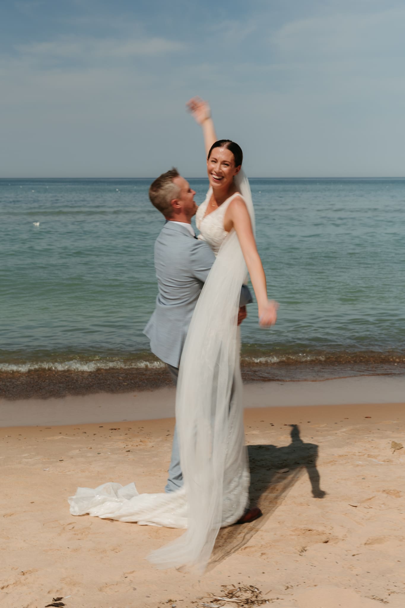 Groom lifts bride in the air and spins her around during their Lake Michigan beach elopement