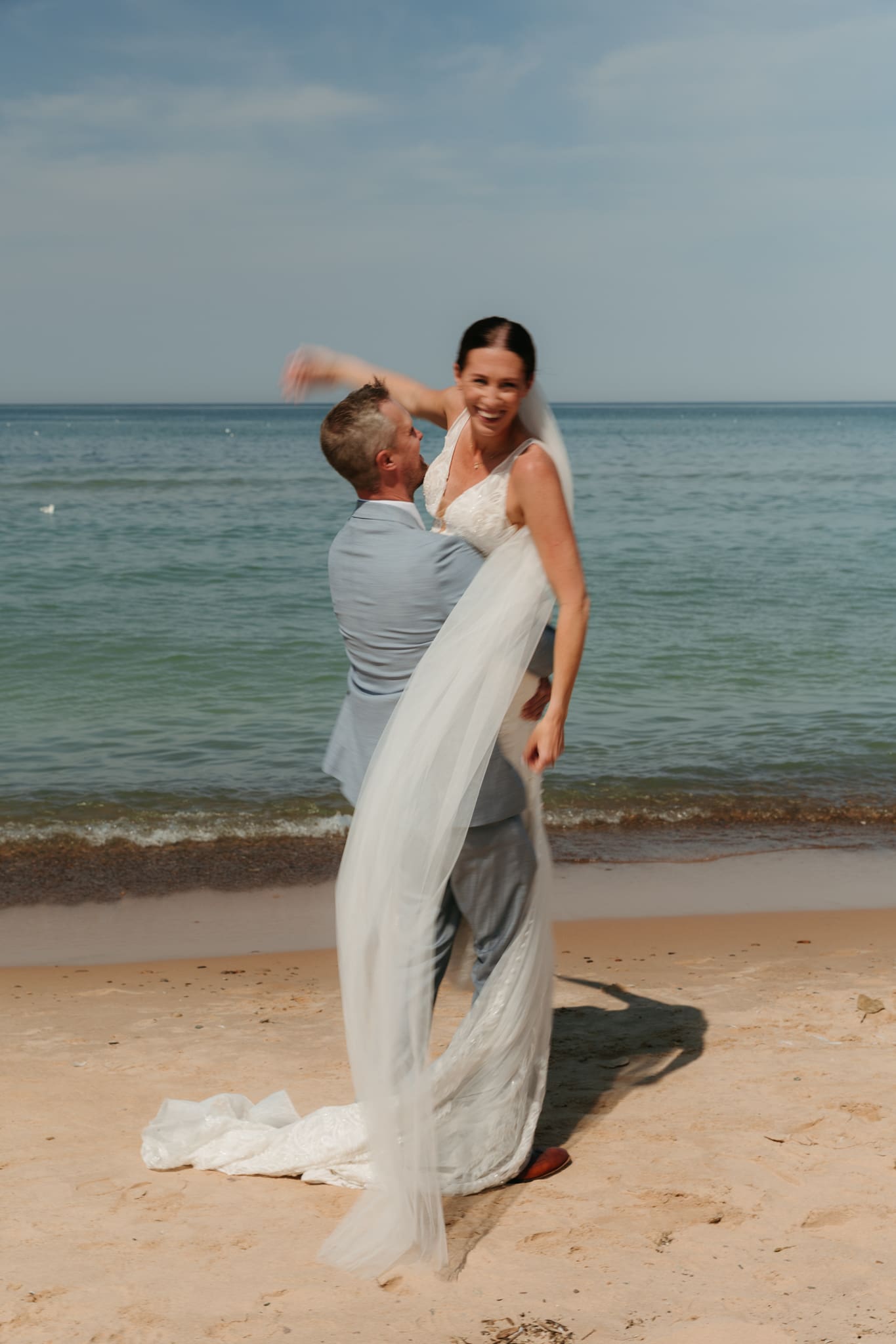 Groom lifts bride in the air and spins her around during their Lake Michigan beach elopement