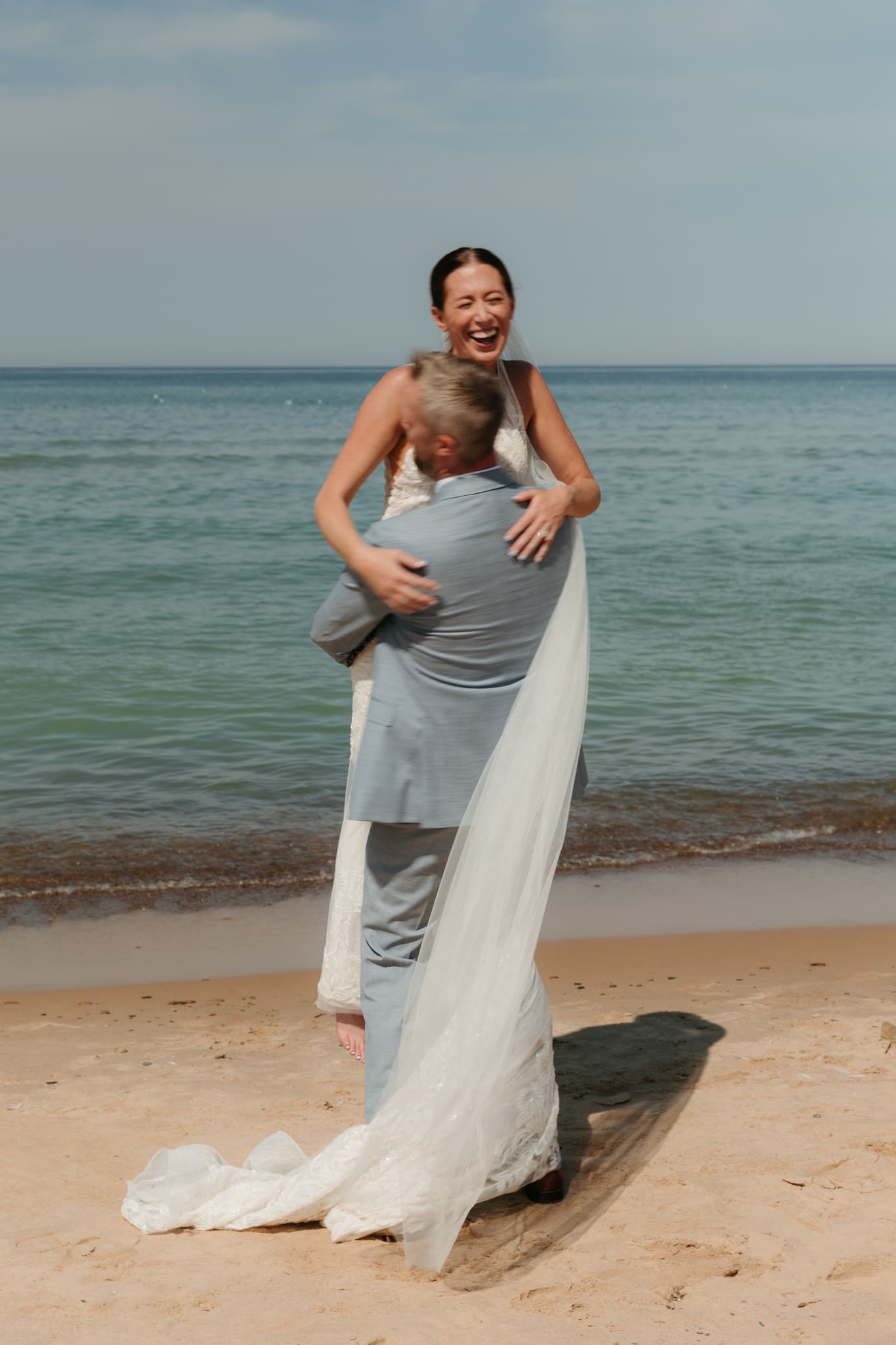 Groom lifts bride in the air and spins her around during their Lake Michigan beach elopement